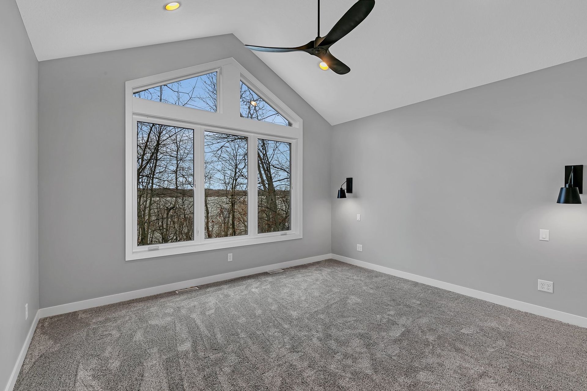 An empty bedroom with a ceiling fan and a large window.