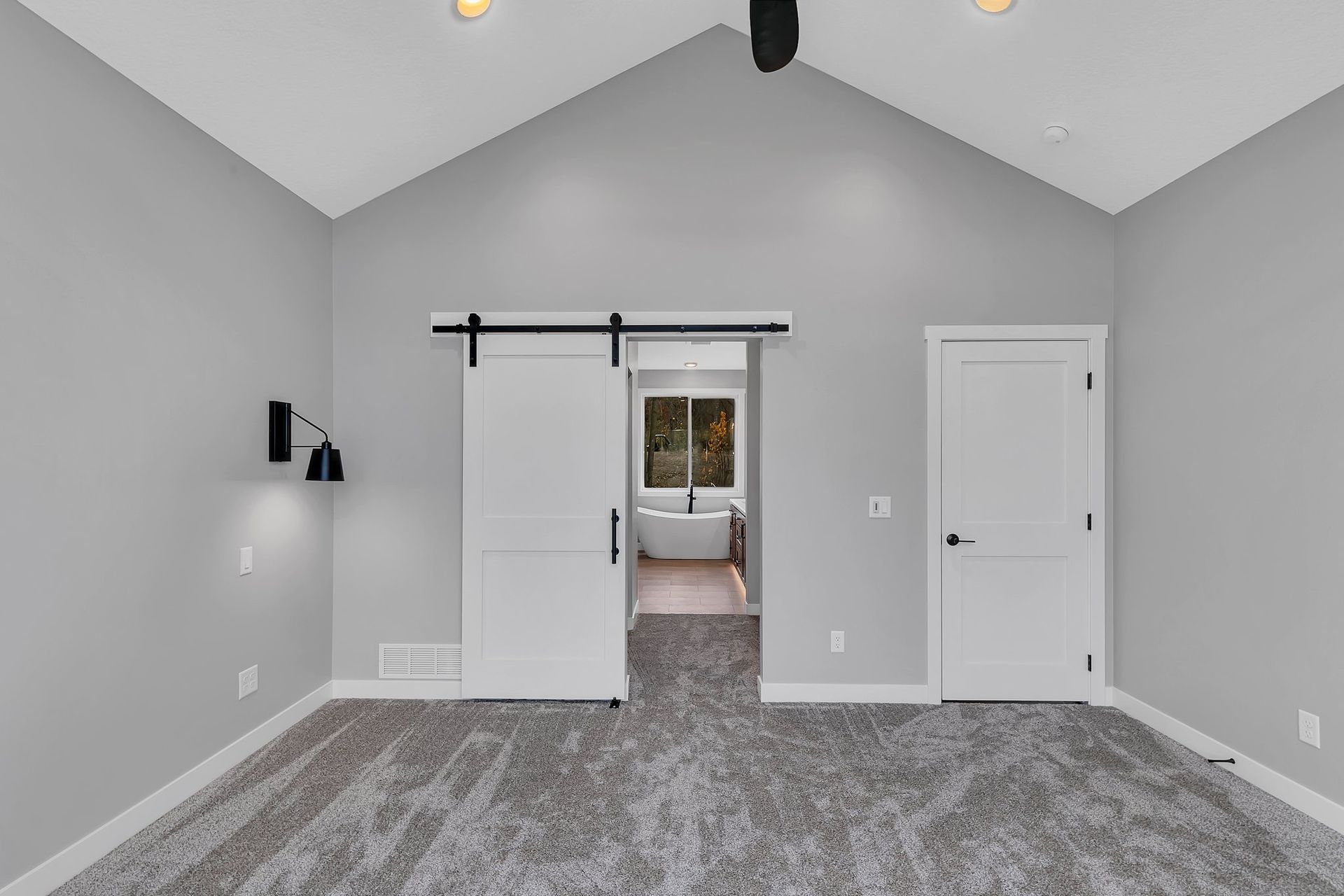 An empty bedroom with a sliding barn door leading to a bathroom.