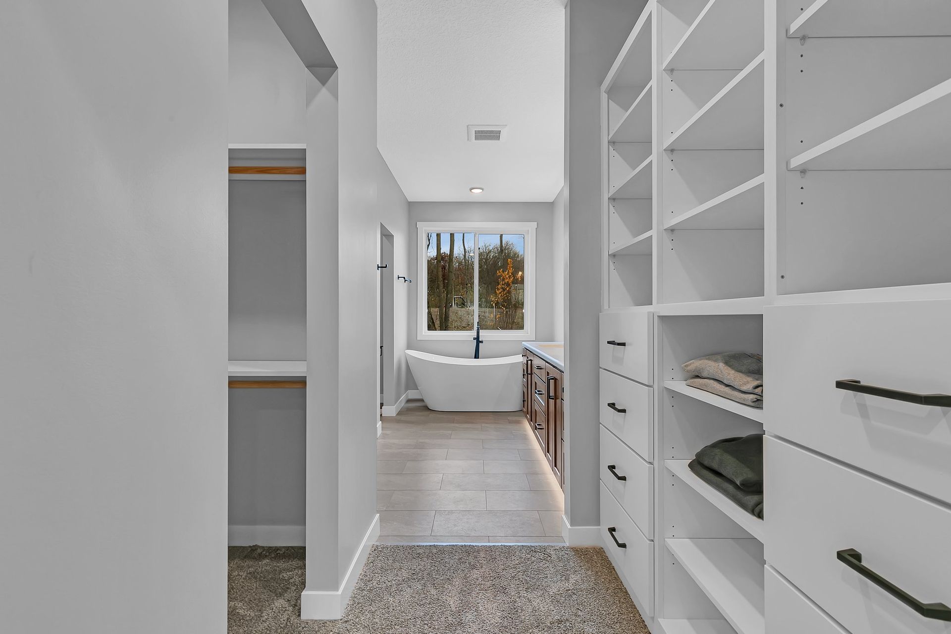 A walk in closet leading to a bathroom with a tub.