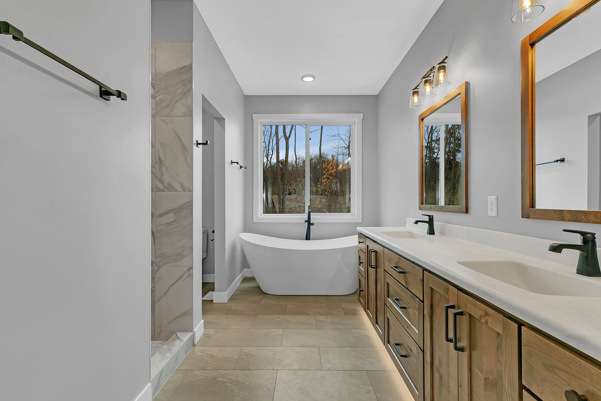 A bathroom with two sinks , a tub , a mirror and a window.