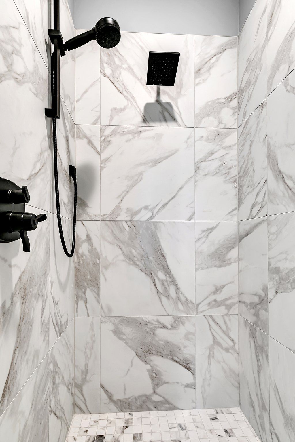 A shower with marble tiles and a black shower head.