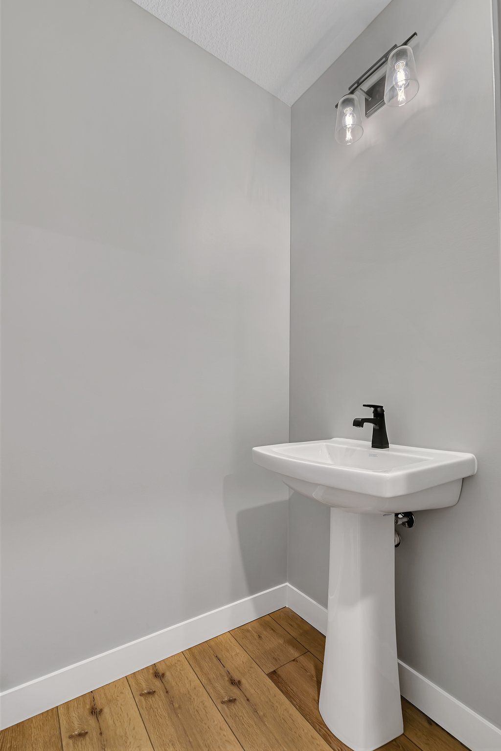 A bathroom with a pedestal sink and wooden floor.