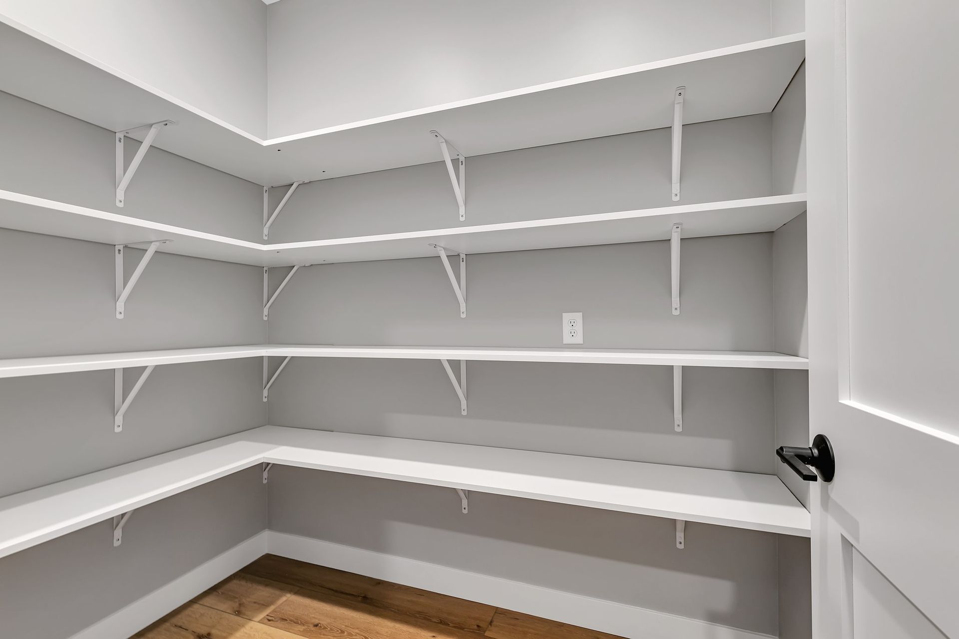 An empty pantry with white shelves and wooden floors.