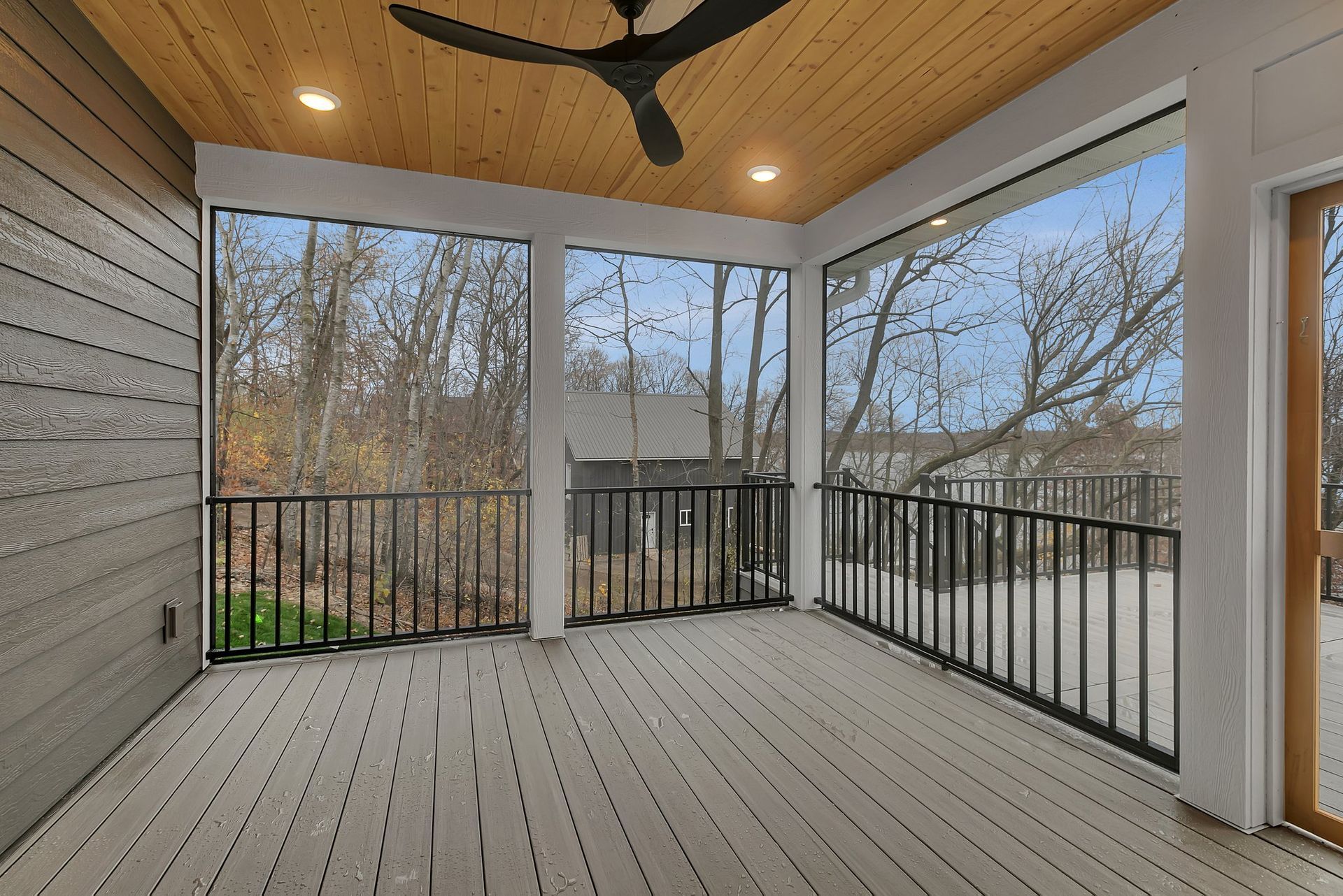 A screened in porch with a ceiling fan and a view of trees.