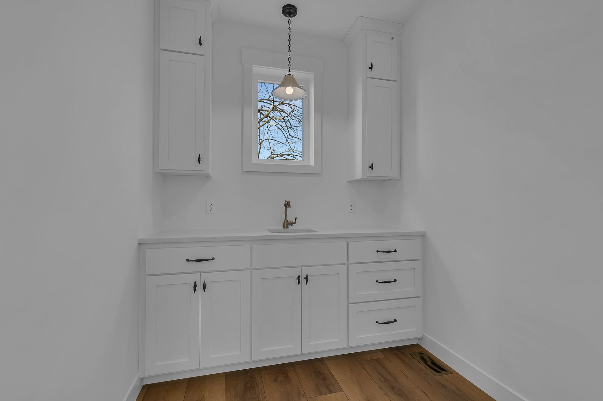 A kitchen with white cabinets , drawers , a sink and a window.