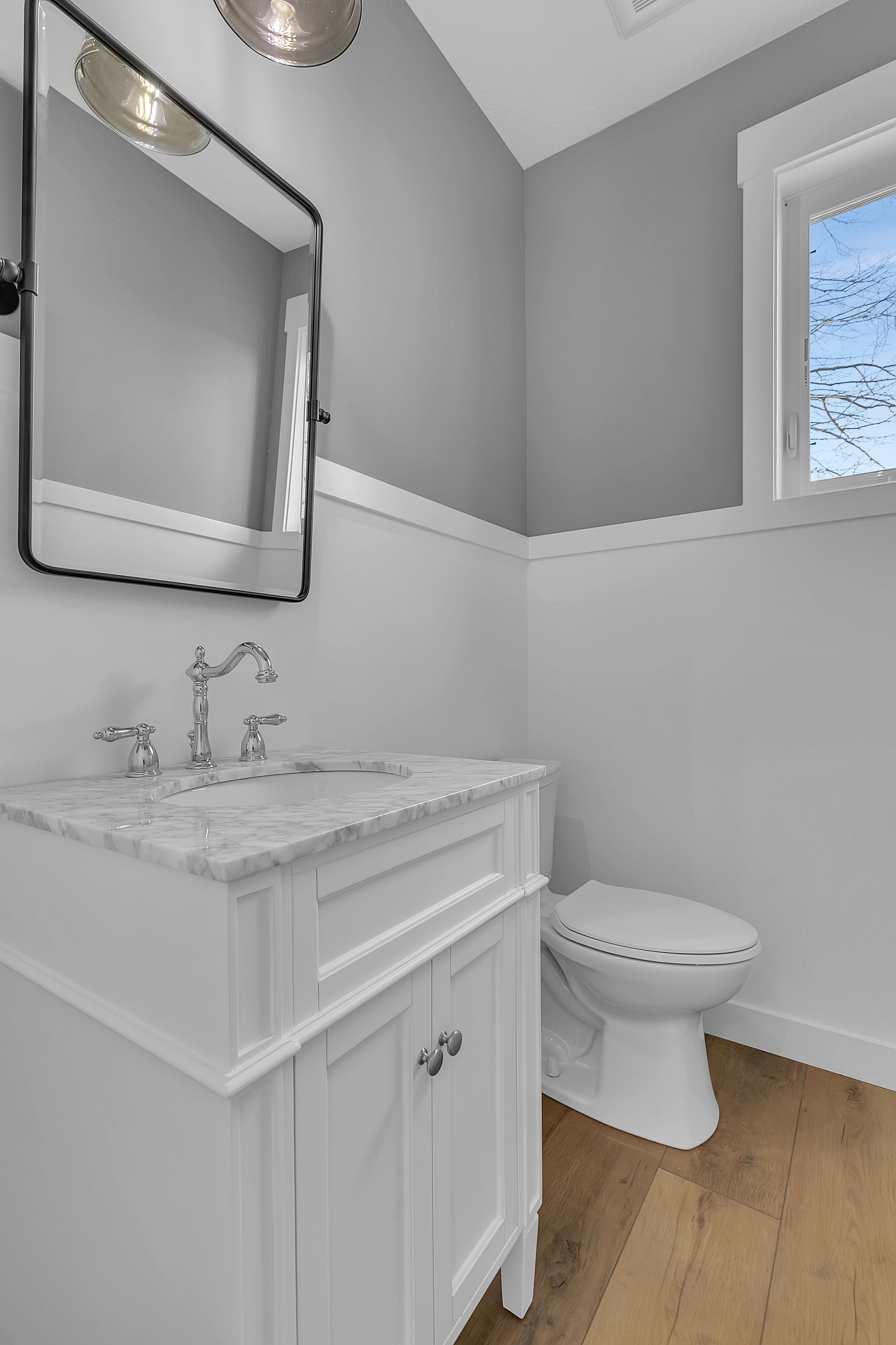 A bathroom with a sink , toilet , mirror and window.