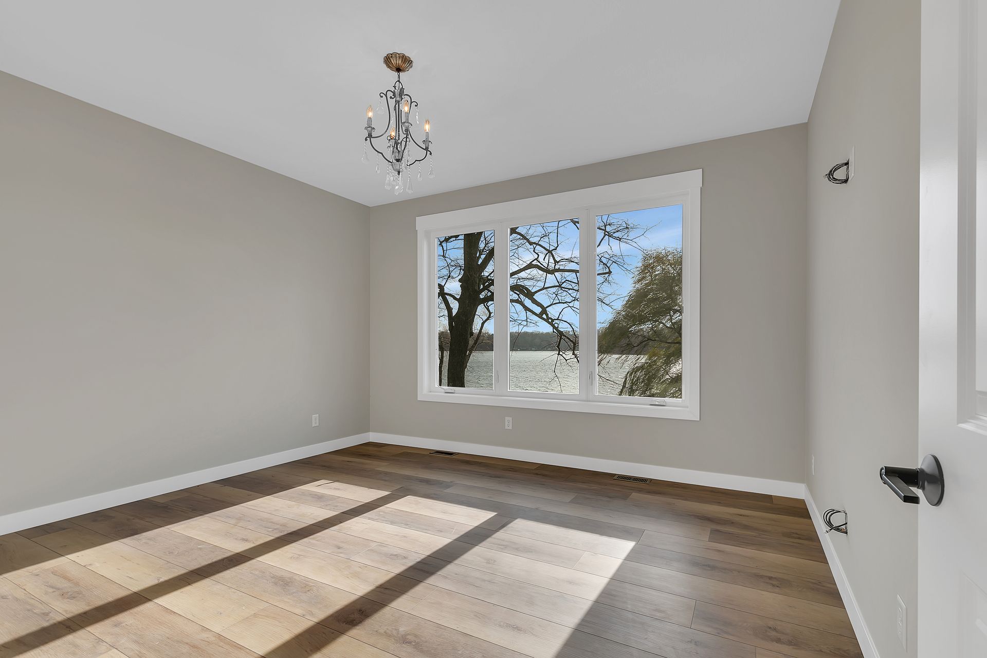 An empty room with two windows and a chandelier hanging from the ceiling.