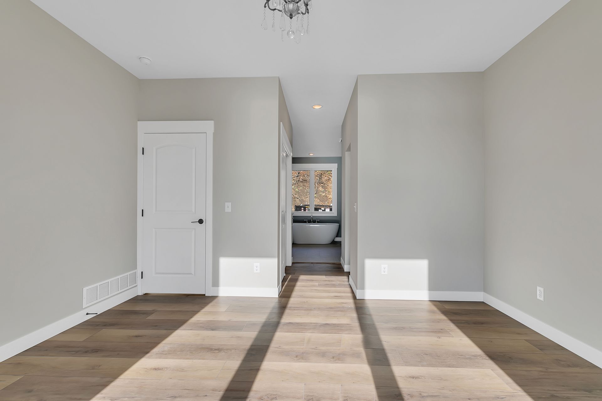 An empty room with hardwood floors and a bathtub in the background