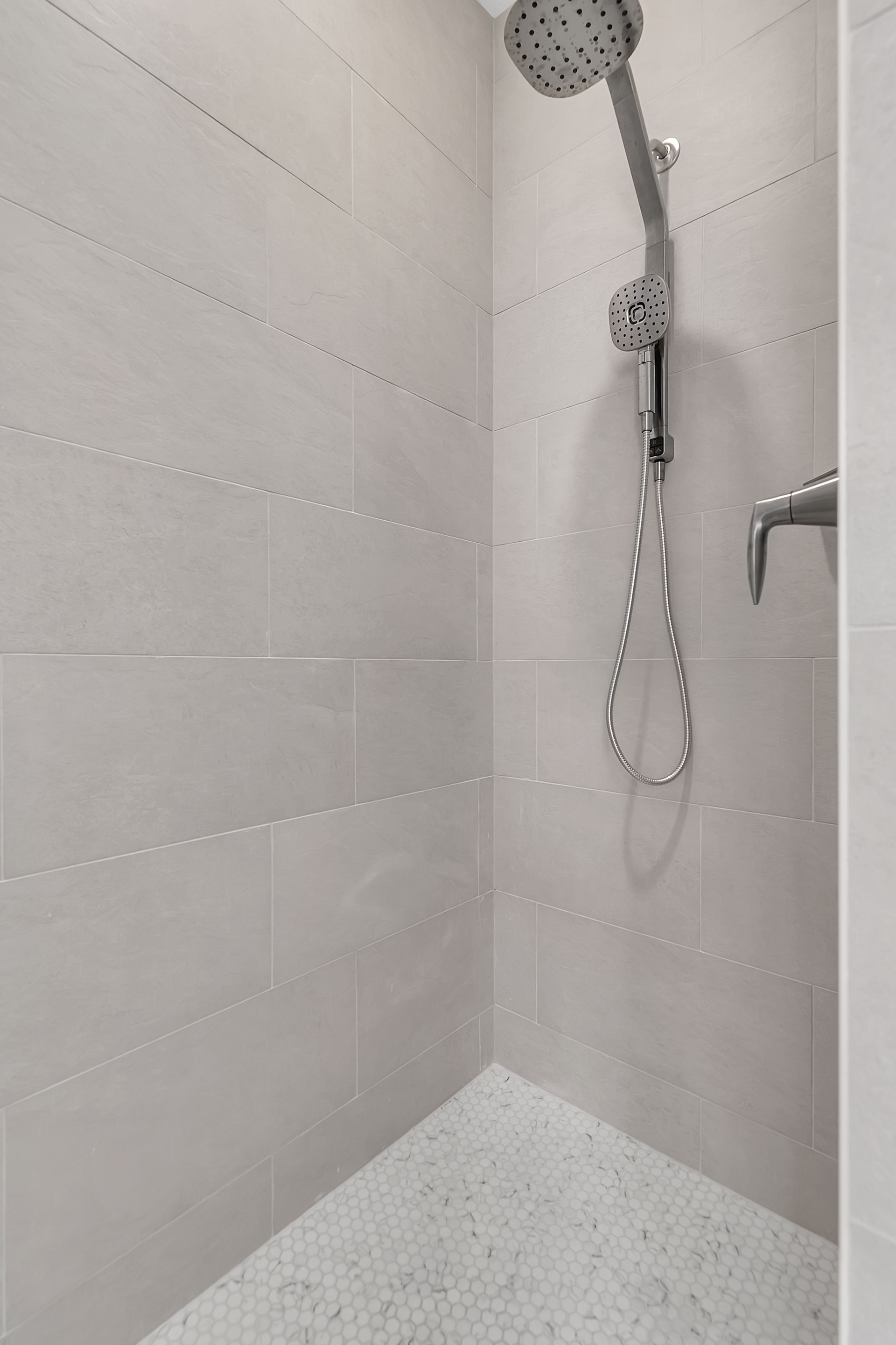 A shower with a shower head and a white tile floor.