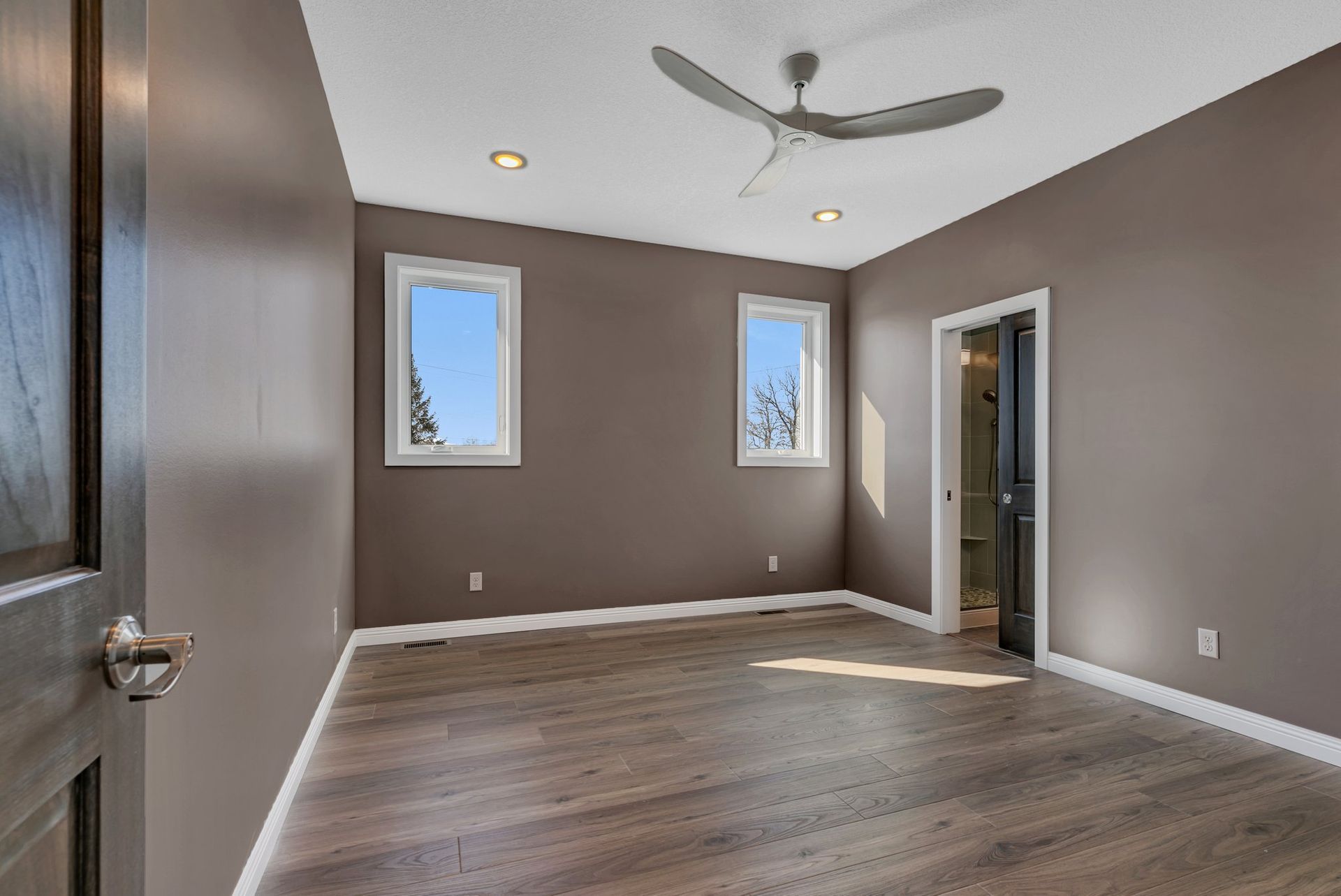 An empty room with a ceiling fan and two windows.