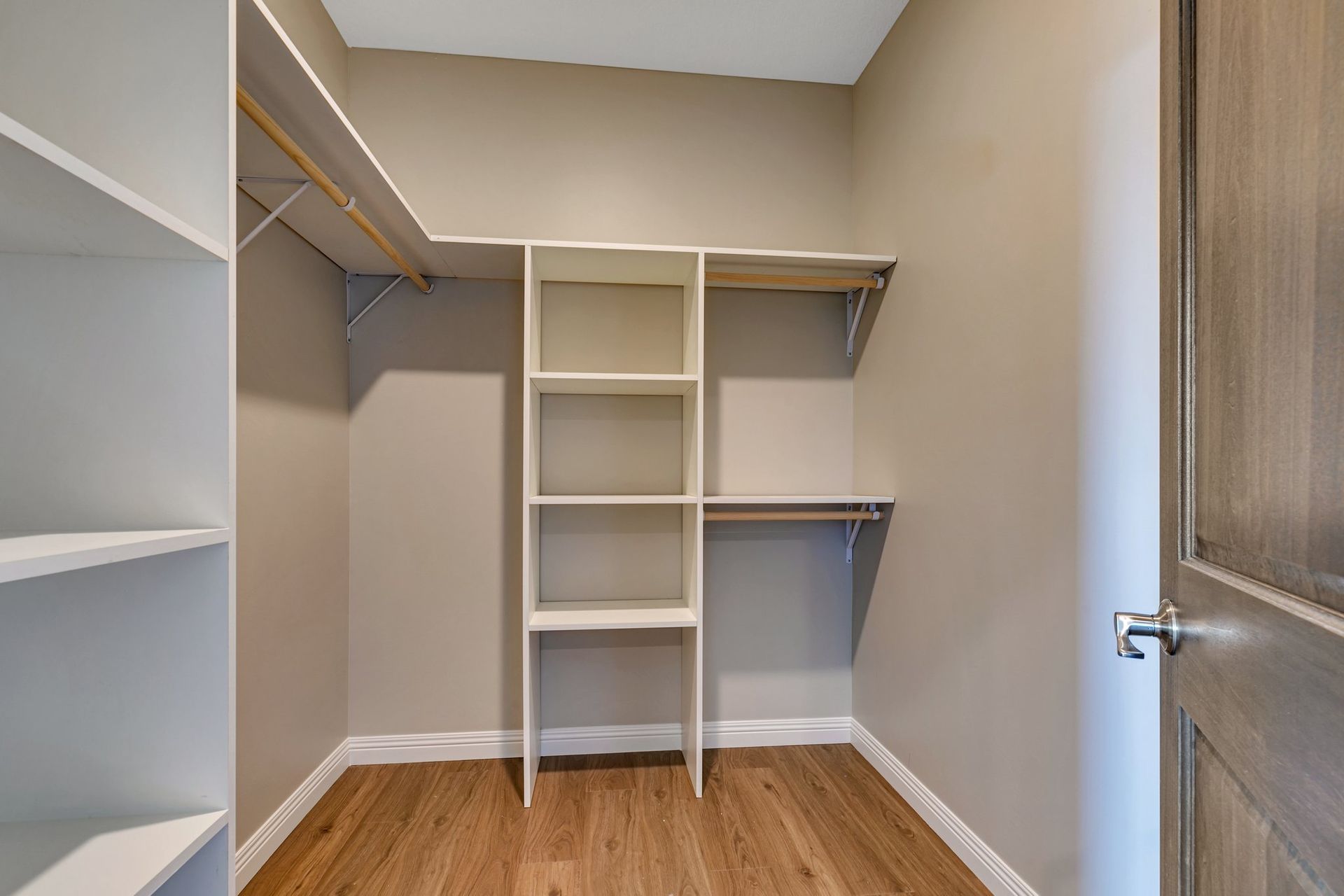 An empty walk in closet with wooden floors and shelves.