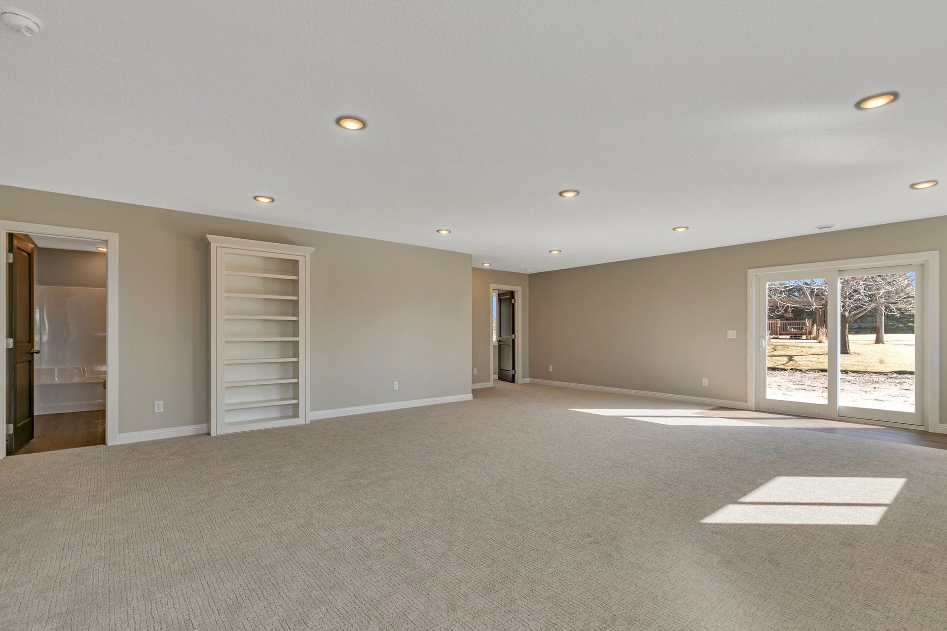 A large empty room with a carpeted floor and sliding glass doors.