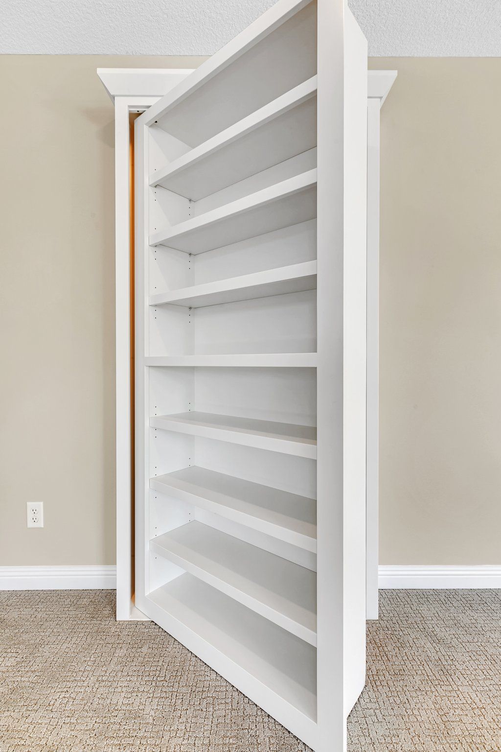 A white bookshelf is hidden behind a door in a room.