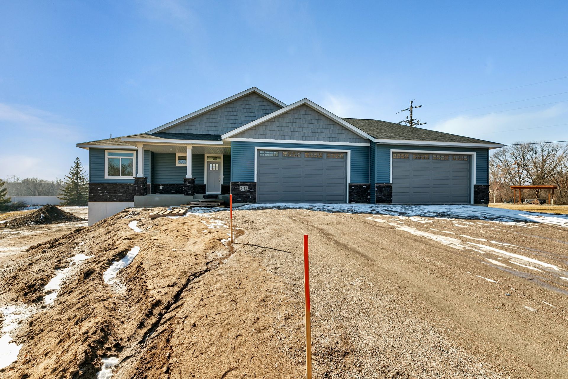 A house with two garages is sitting on top of a dirt road.