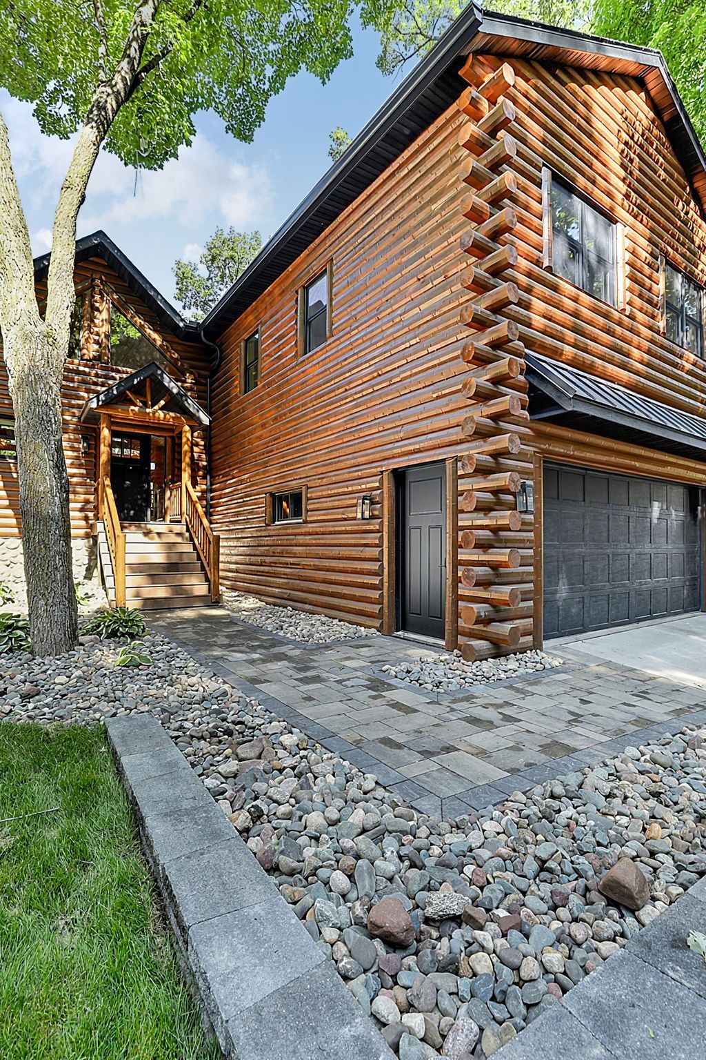 Log cabin-style house exterior with stone driveway and garage under trees