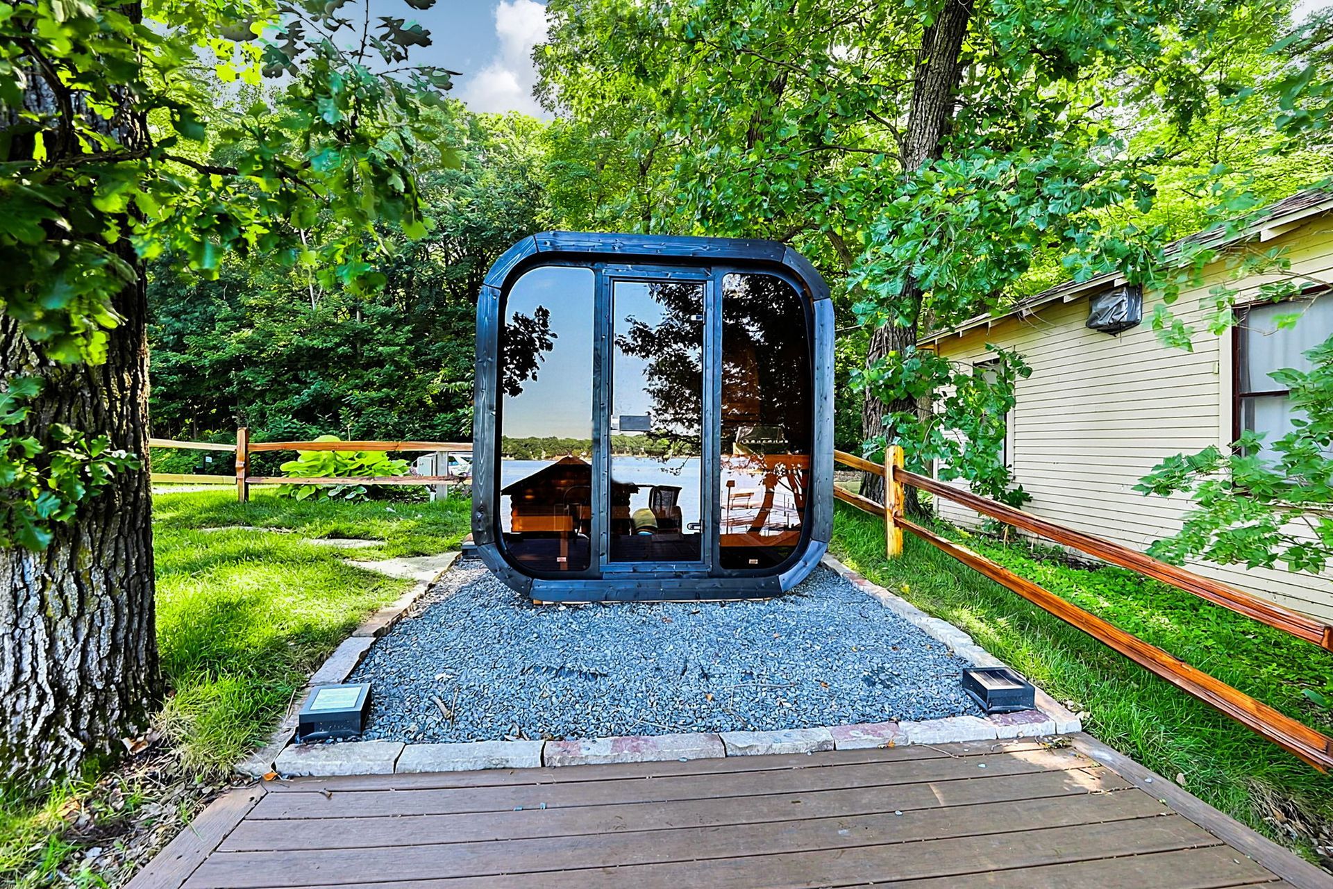Modern glass pod on gravel patio in a leafy garden with trees and house nearby