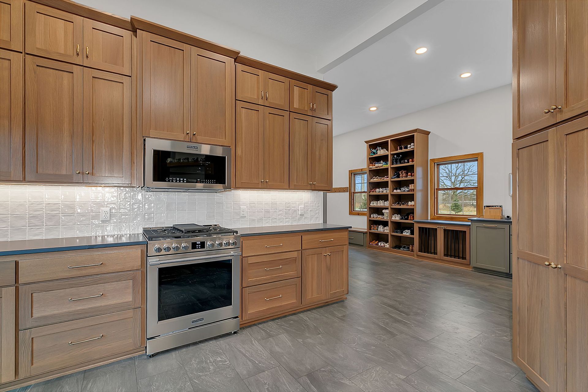 Kitchen with wood cabinets, stainless steel appliances, white tile backsplash, and concrete floor.