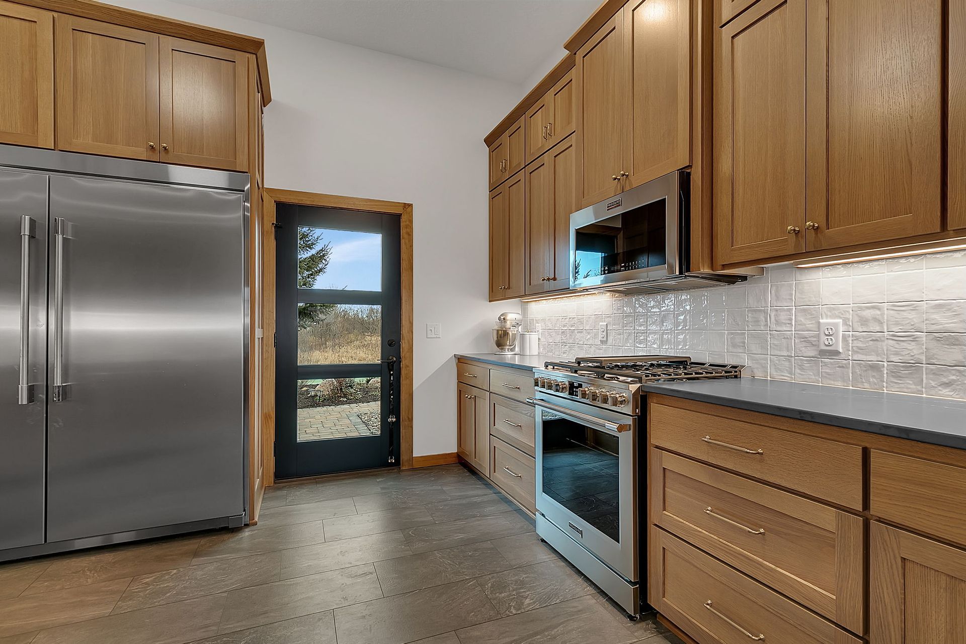 Kitchen with stainless steel appliances, oak cabinets, and a door leading outside.