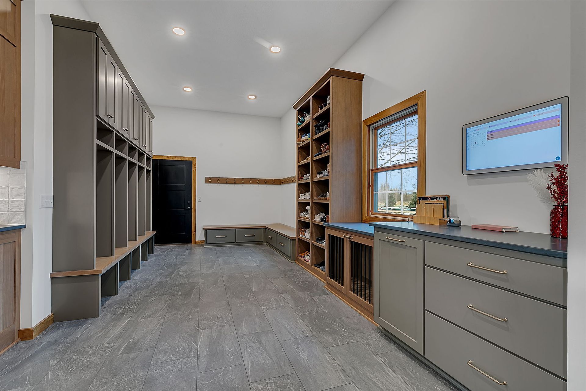 Mudroom with built-in lockers, shoe storage, and cabinetry. Gray and wood tones, with a bench, window, and TV.