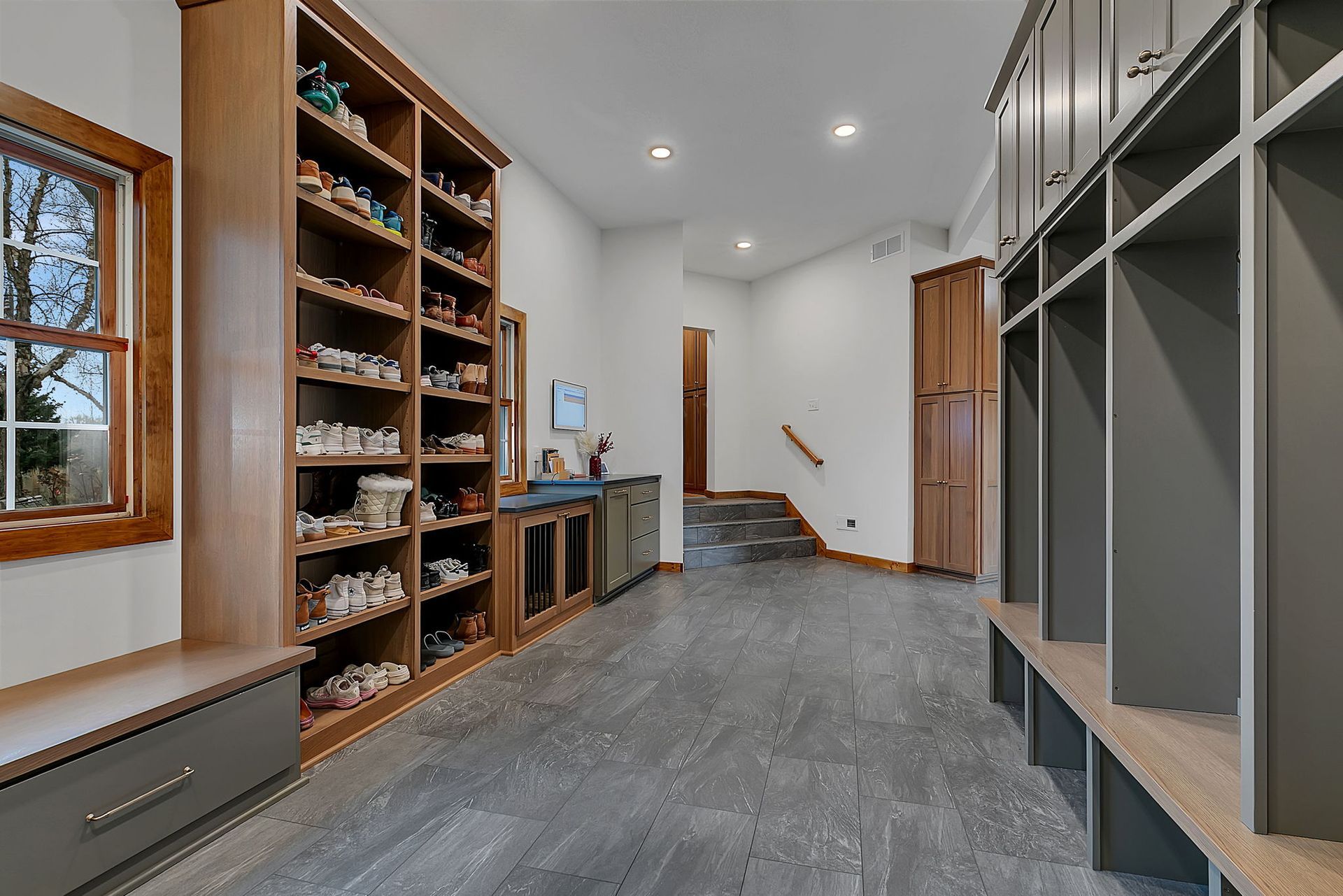 Mudroom with built-in shoe shelves, lockers, bench, and window. Gray and wood tones dominate.