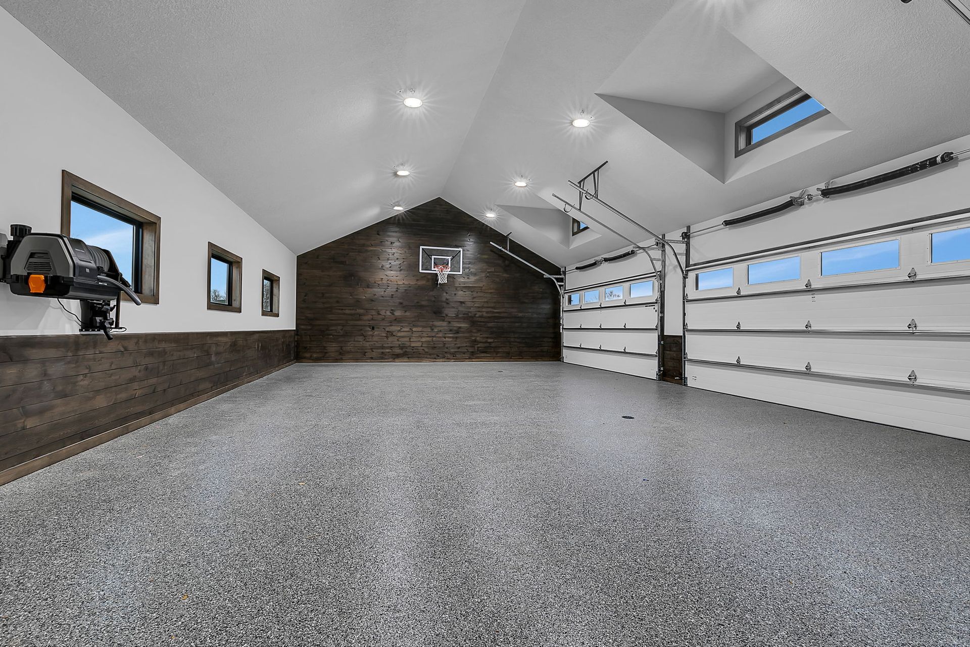 Spacious garage with basketball hoop, epoxy floor, and garage door with windows.