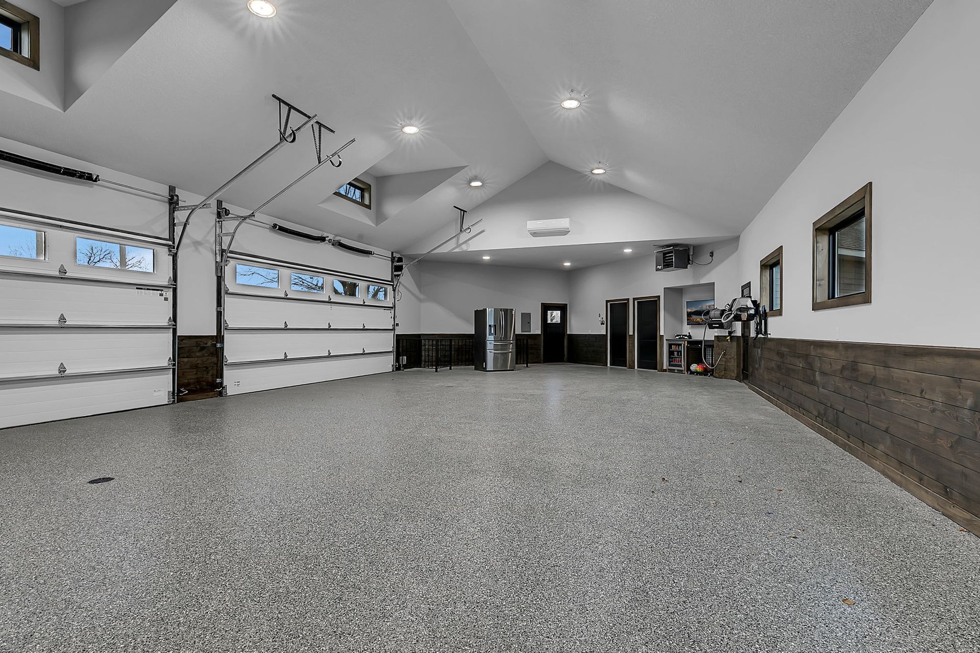 Spacious garage with epoxy floor, three garage doors, and dark wood accents.