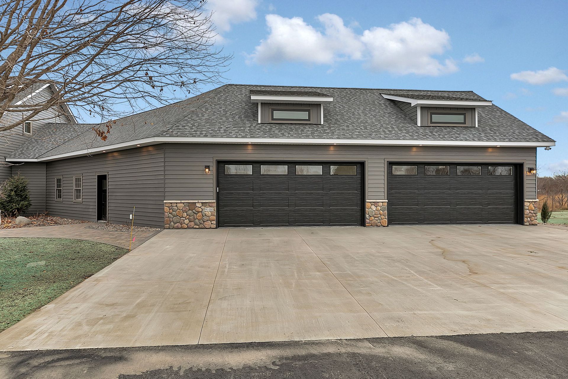 Gray garage with two bays, stone accents, and a long concrete driveway under a cloudy sky.