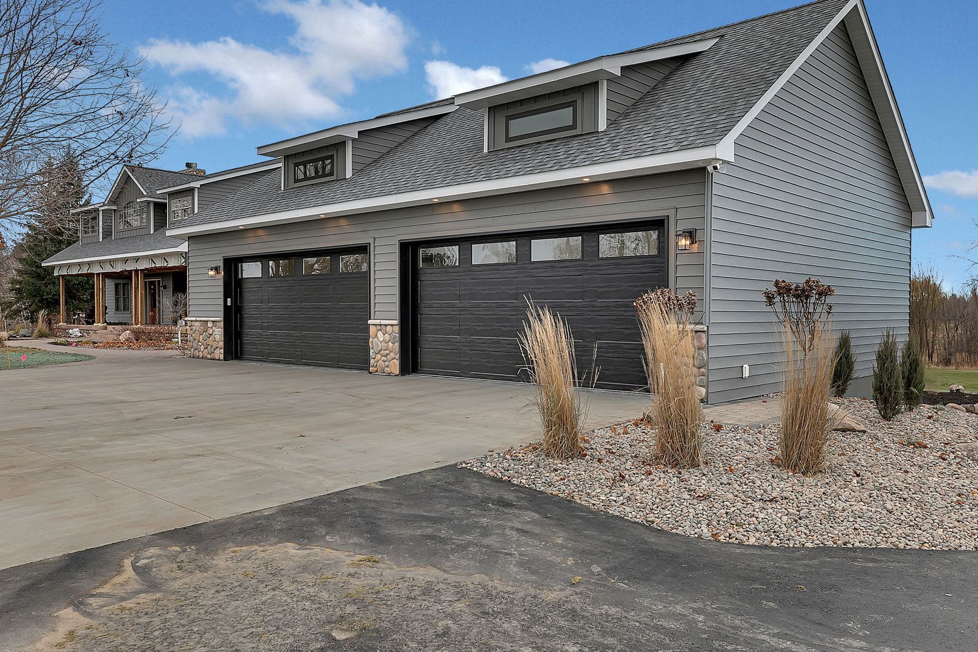 Two-car garage with gray siding, black garage doors, and a driveway on a sunny day.