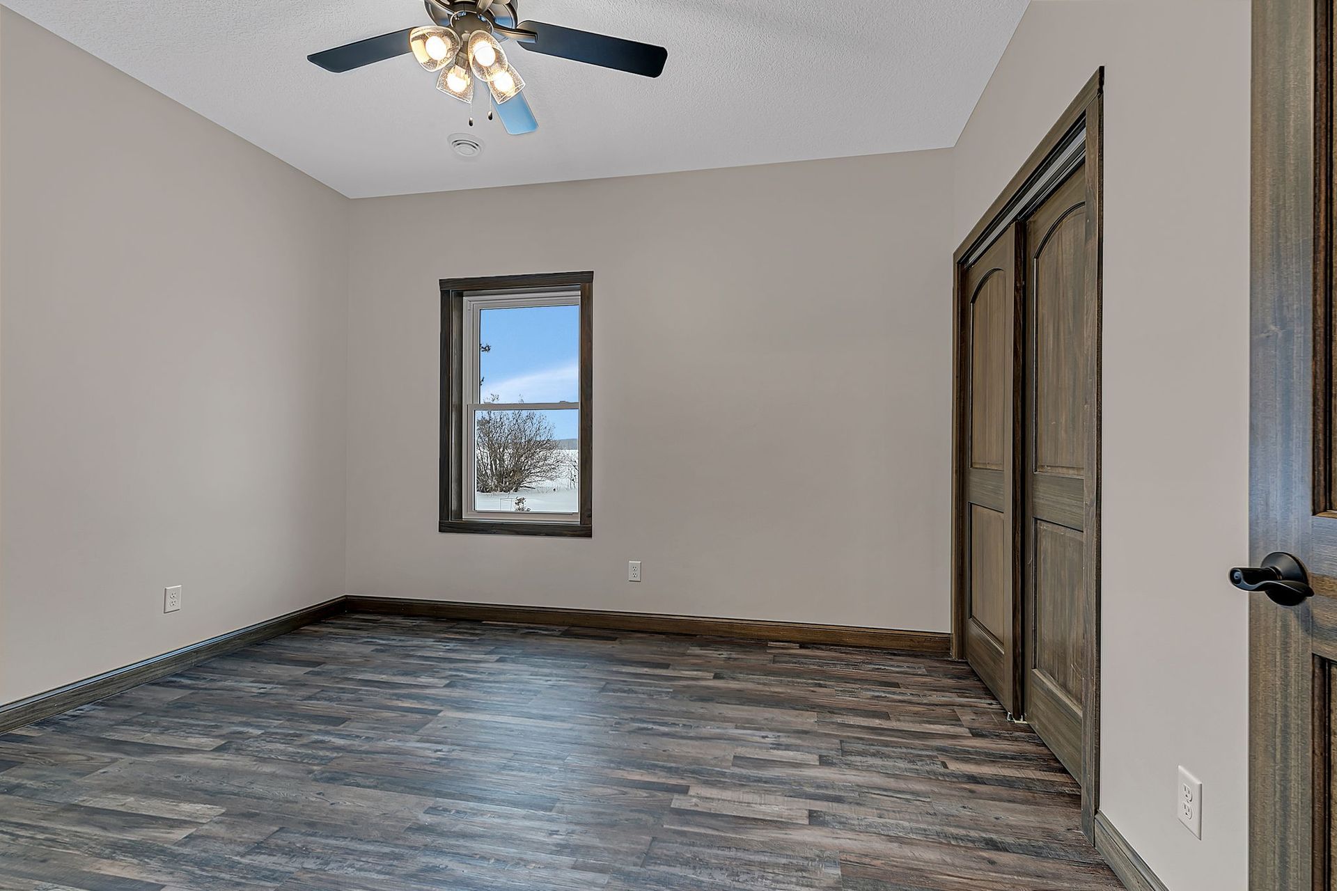 Empty bedroom with gray walls, dark wood-look floor, window, and sliding closet doors.