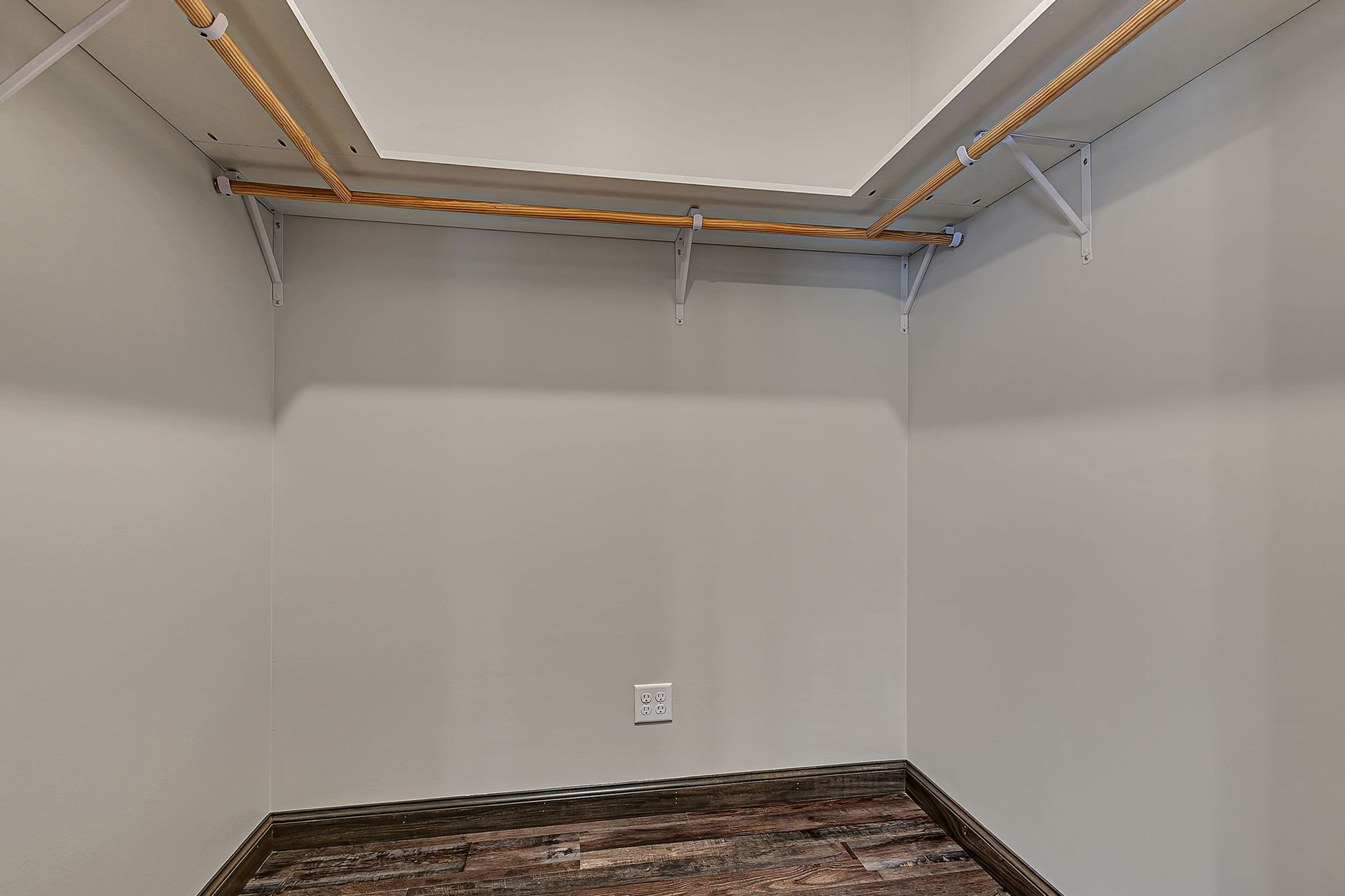 Empty closet with a shelf, white walls, and wood-look flooring.