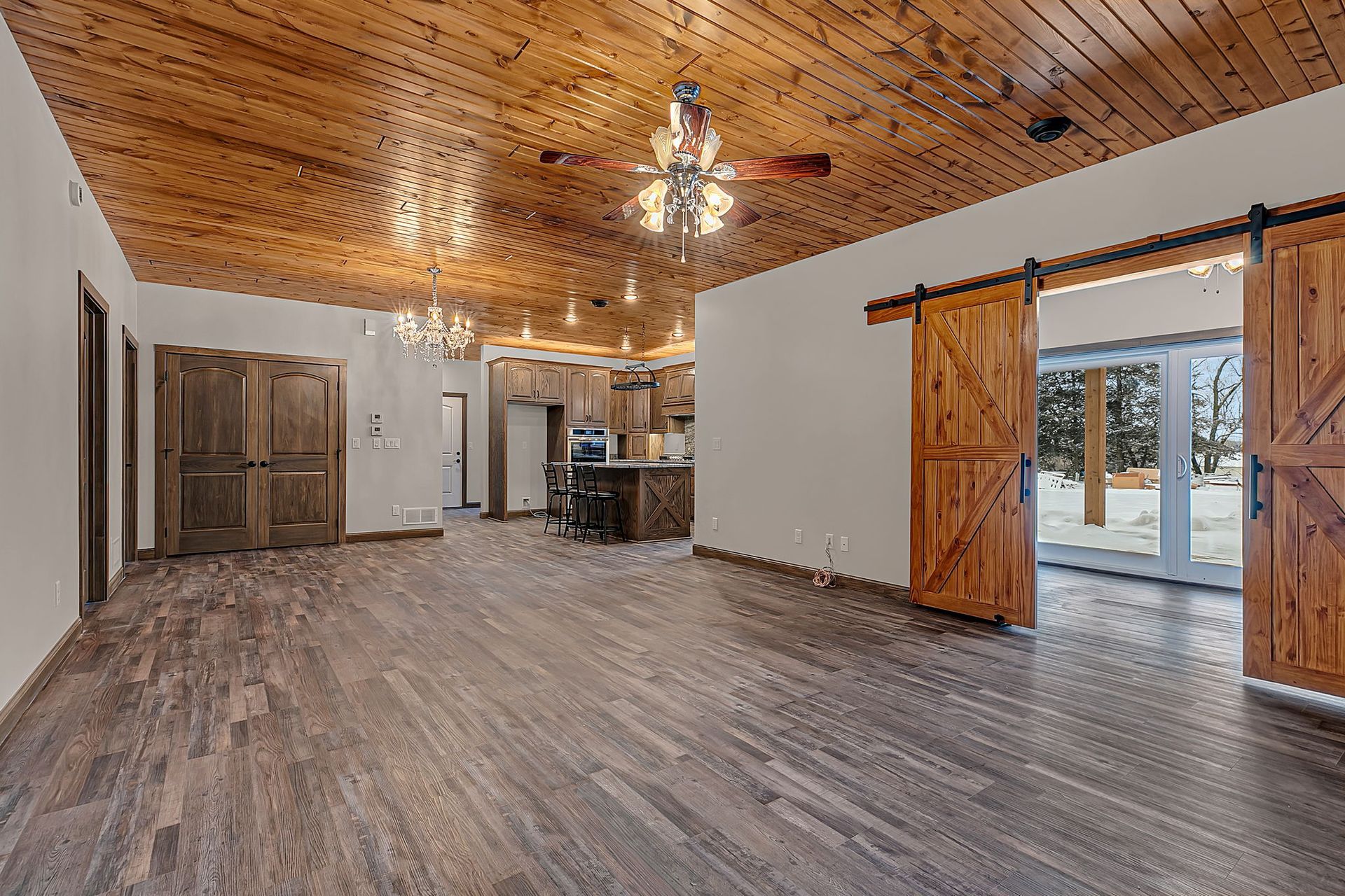 Wooden ceiling and floors in an open-plan room with sliding barn doors and kitchen visible.