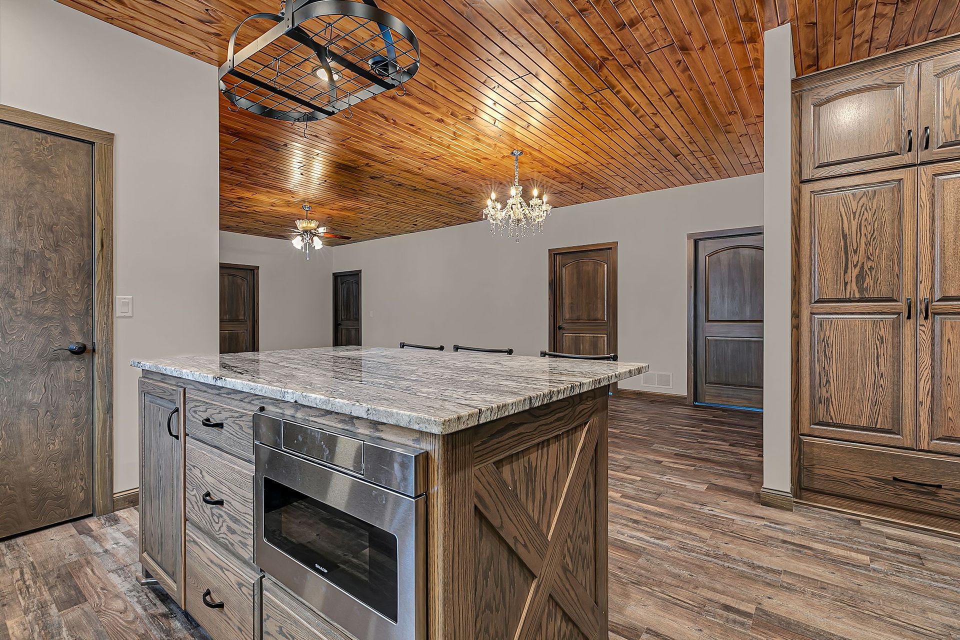 Kitchen with wooden cabinets, island with microwave, wood ceiling, and granite countertop.
