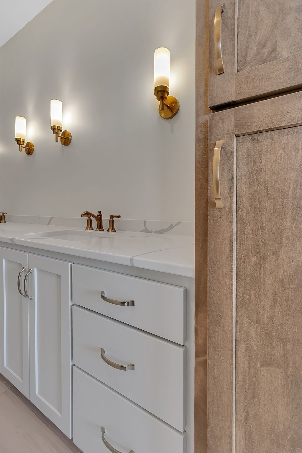 Bathroom with white vanity, marble countertop, gold fixtures, and wall sconces.