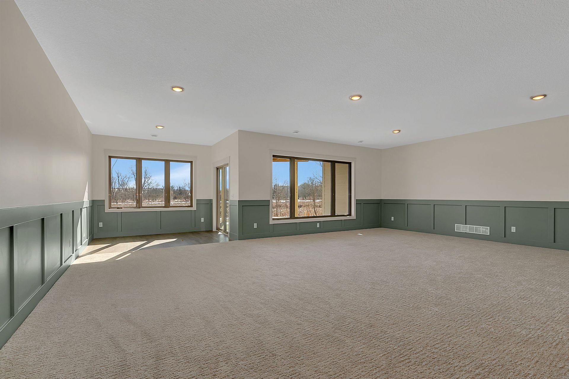 Empty room with beige carpet, green wainscoting, and windows with outdoor views.