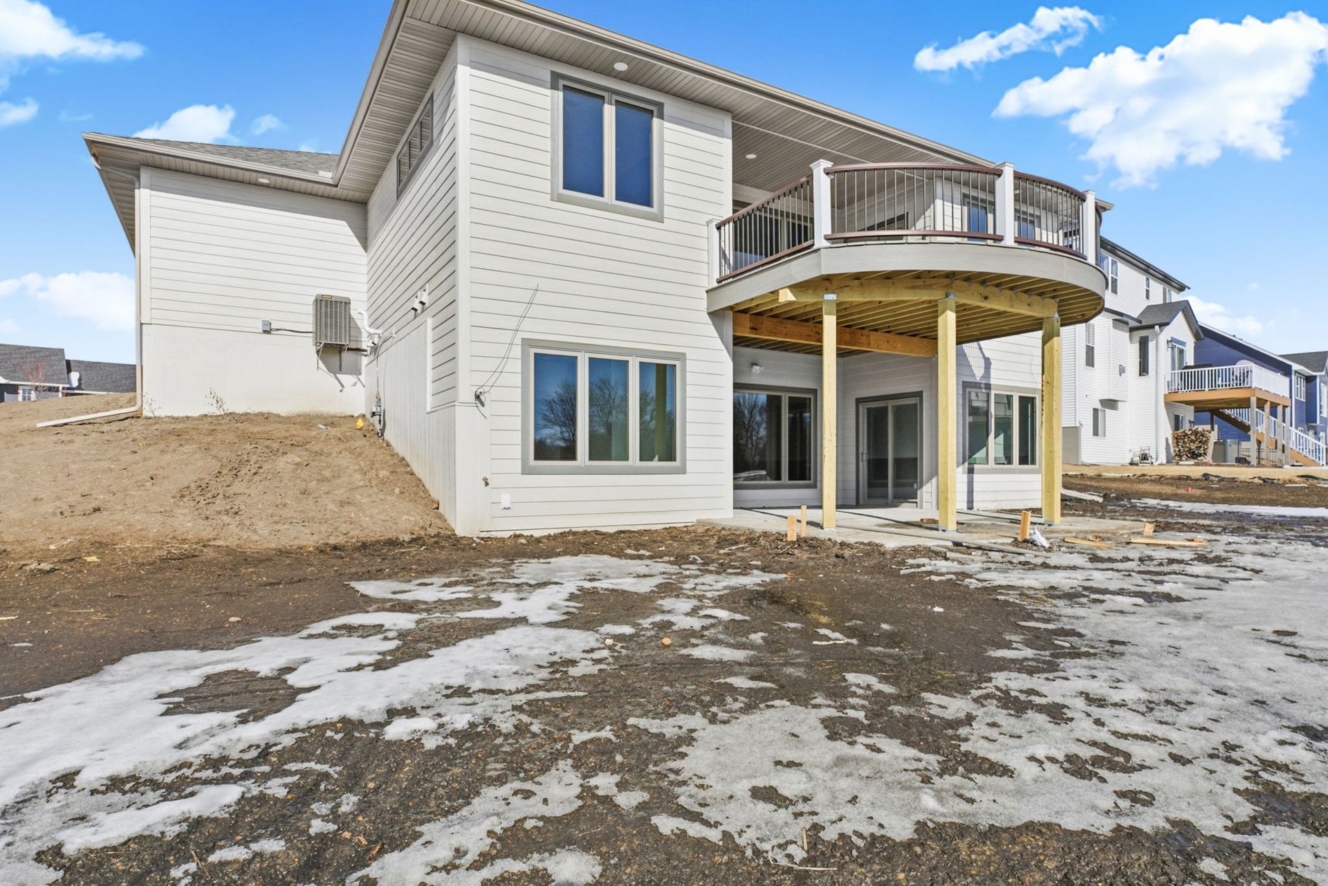 Two-story house with a round deck, white siding, and dirt landscaping in winter.