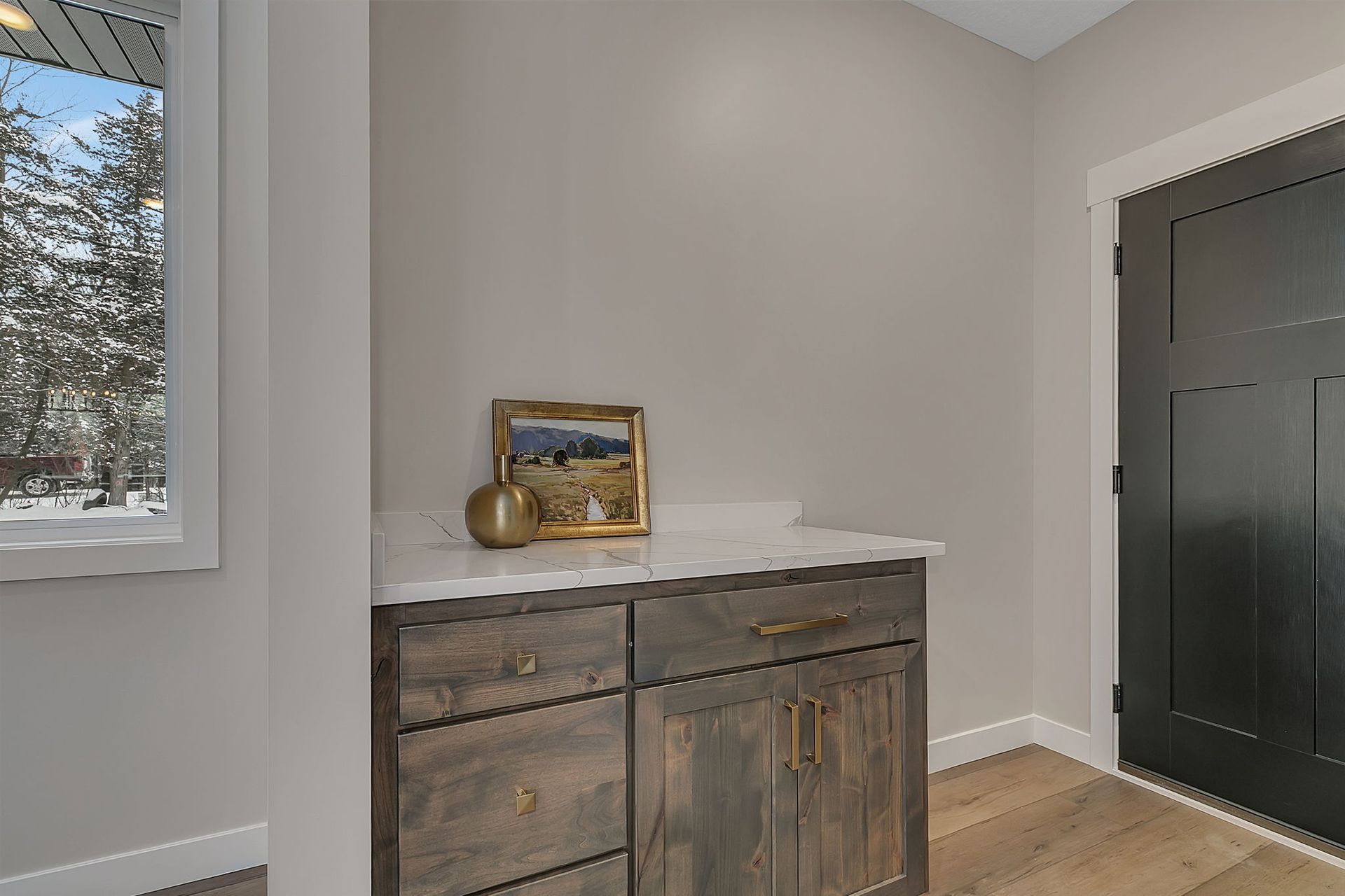 Wooden cabinet with white countertop and artwork in a neutral-toned room near a door and window.