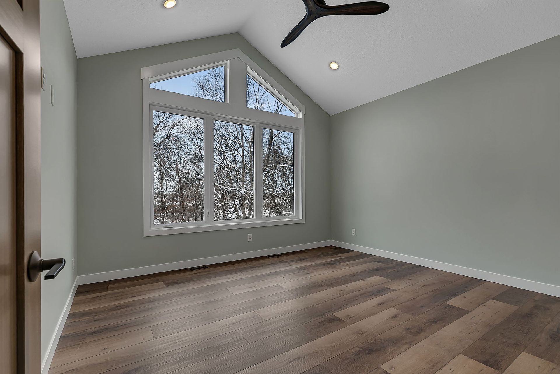Empty room with large windows, vaulted ceiling, and wood flooring. Walls are light green.