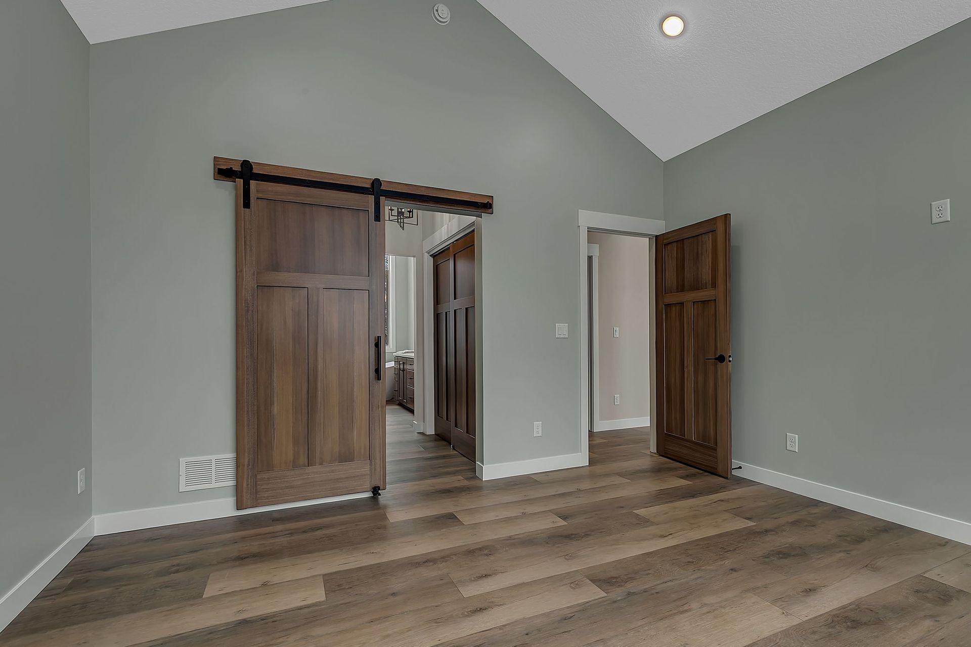 Empty bedroom with wood floors and two brown wooden doors. The walls are gray.
