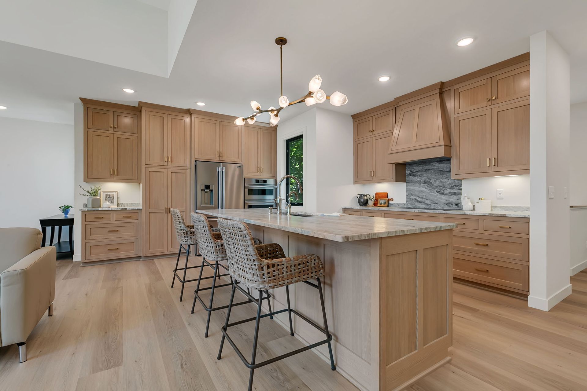 Modern kitchen with light wood cabinets, island seating, stainless appliances, and white countertops