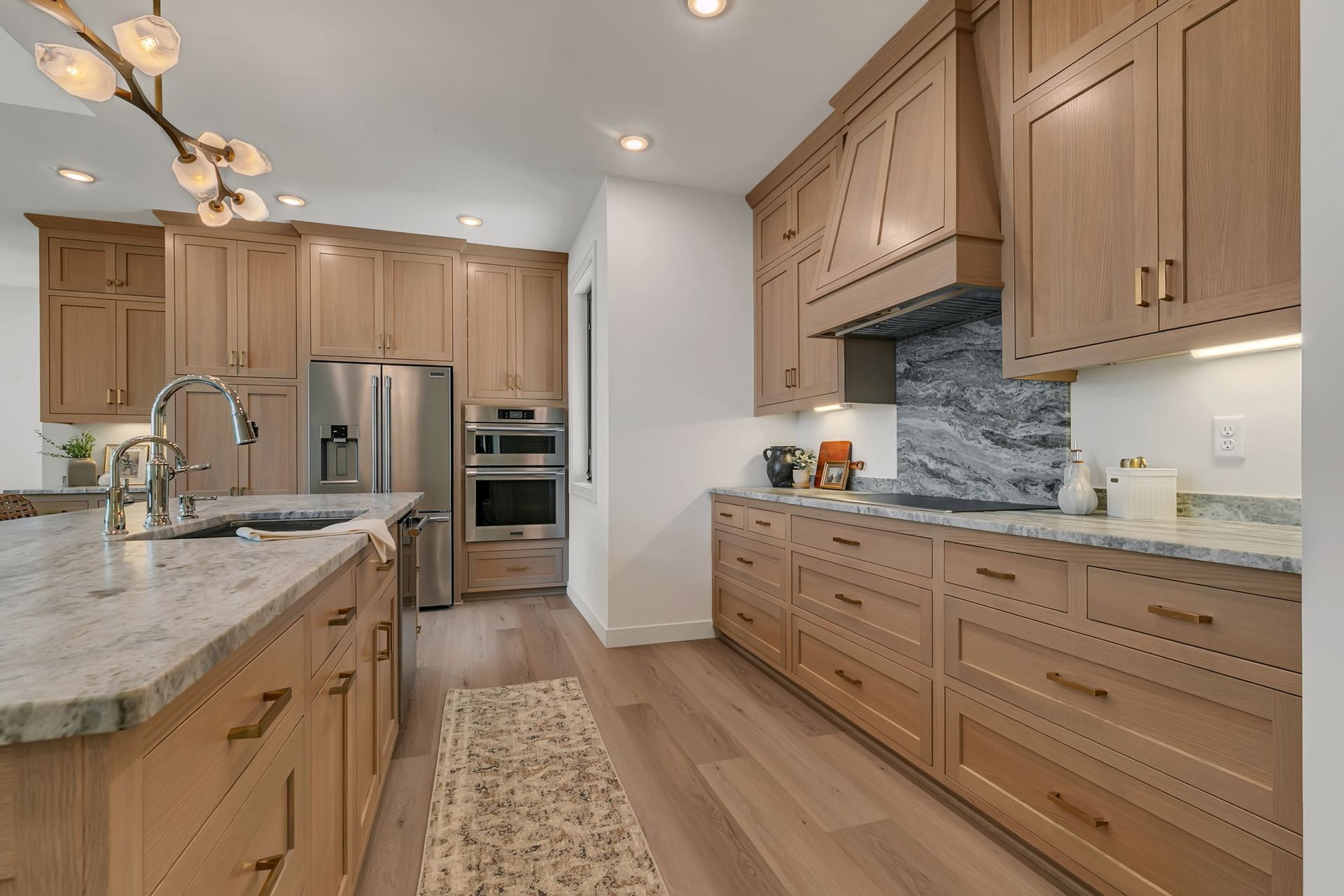 Modern kitchen with wood cabinets, stainless steel appliances, marble island, and light wood floors
