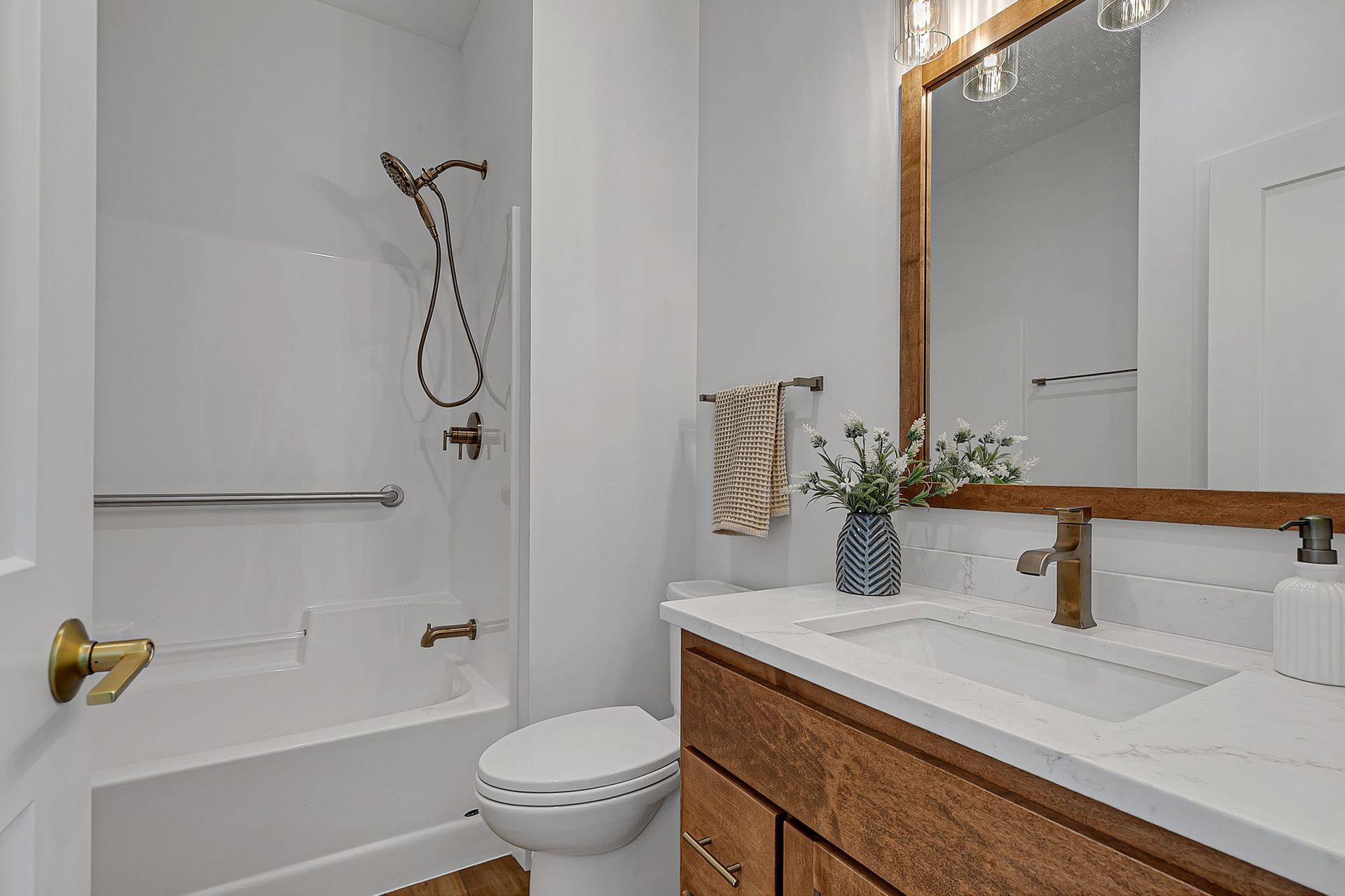 Bathroom with white walls, tub/shower, wooden vanity, and large mirror.