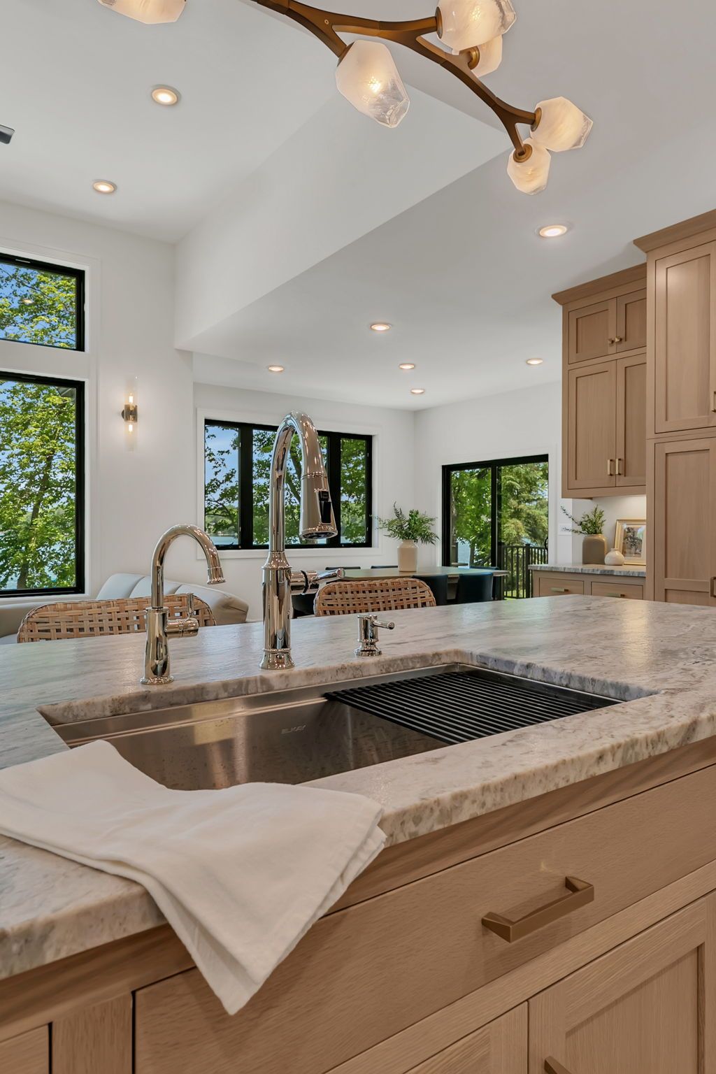 Bright kitchen with a large island sink, tan cabinets, granite countertops, and sunlit windows.