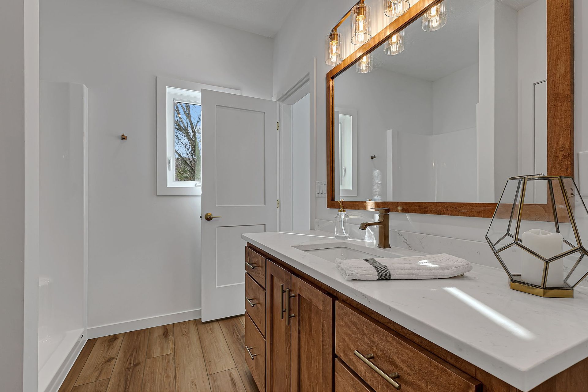 Bathroom with white walls, wooden vanity, and large mirror. Window and door visible.