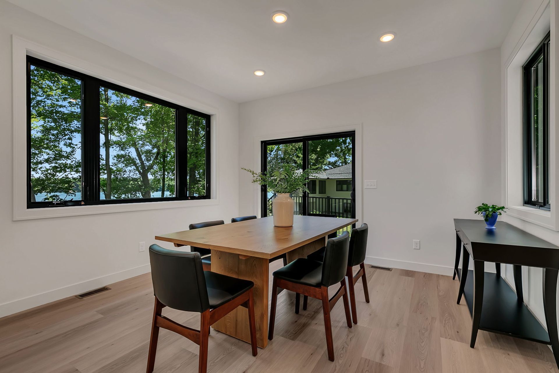 Modern dining room with wooden table, black chairs, large windows, and light wood floors