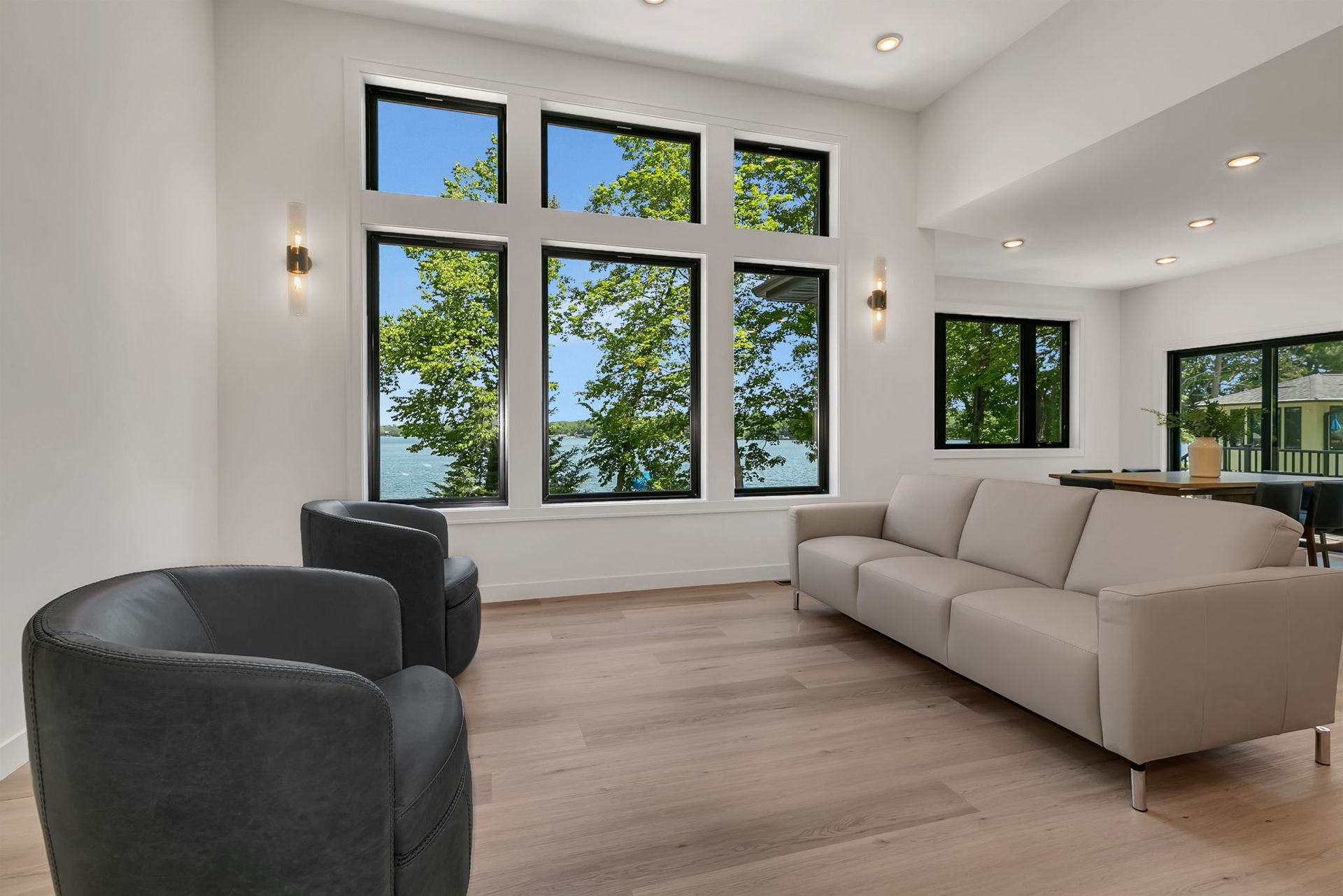 Bright modern living room with large windows, beige sofa, and dark accent chairs