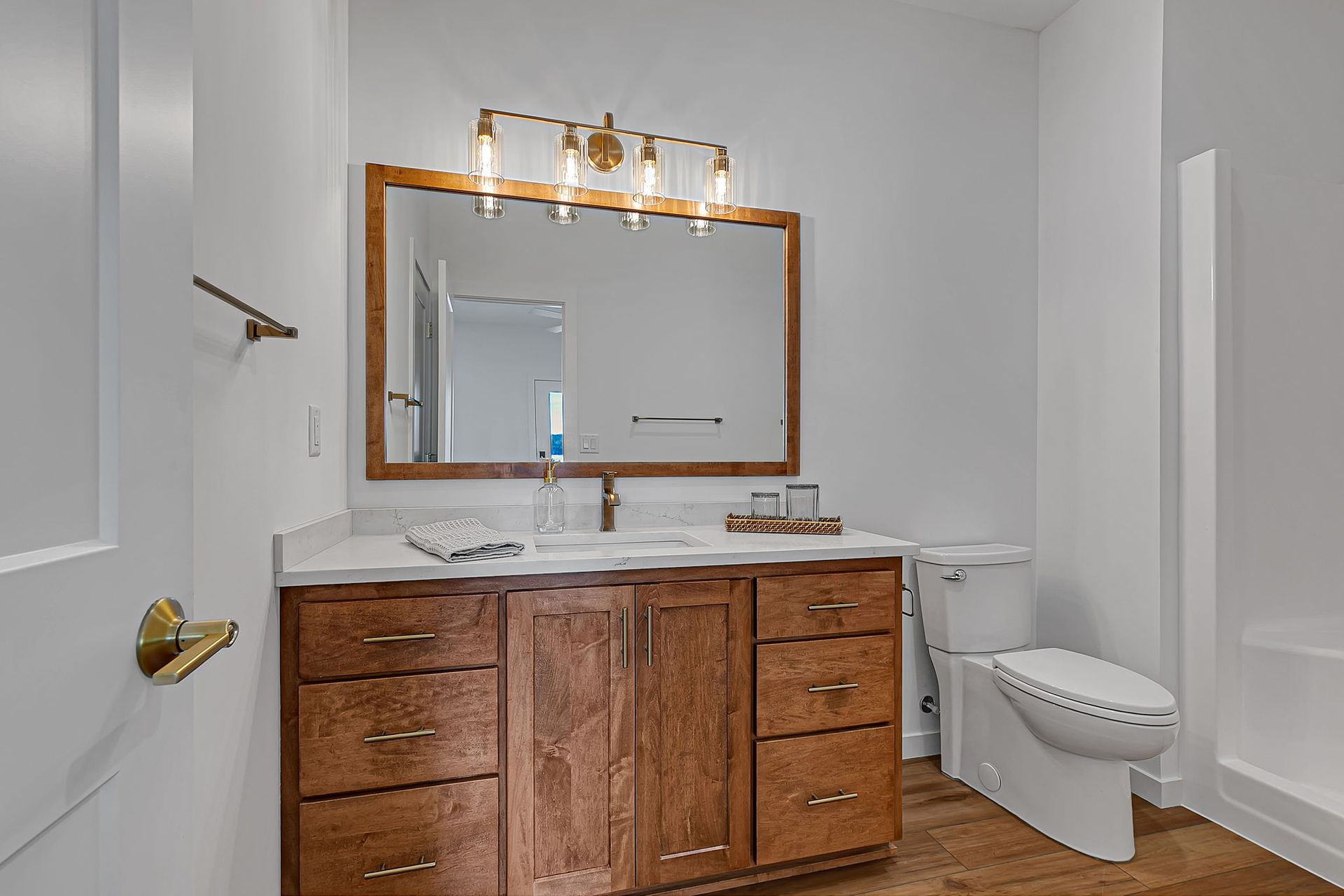 Bathroom with wood vanity, large mirror, and gold fixtures. White walls and toilet.