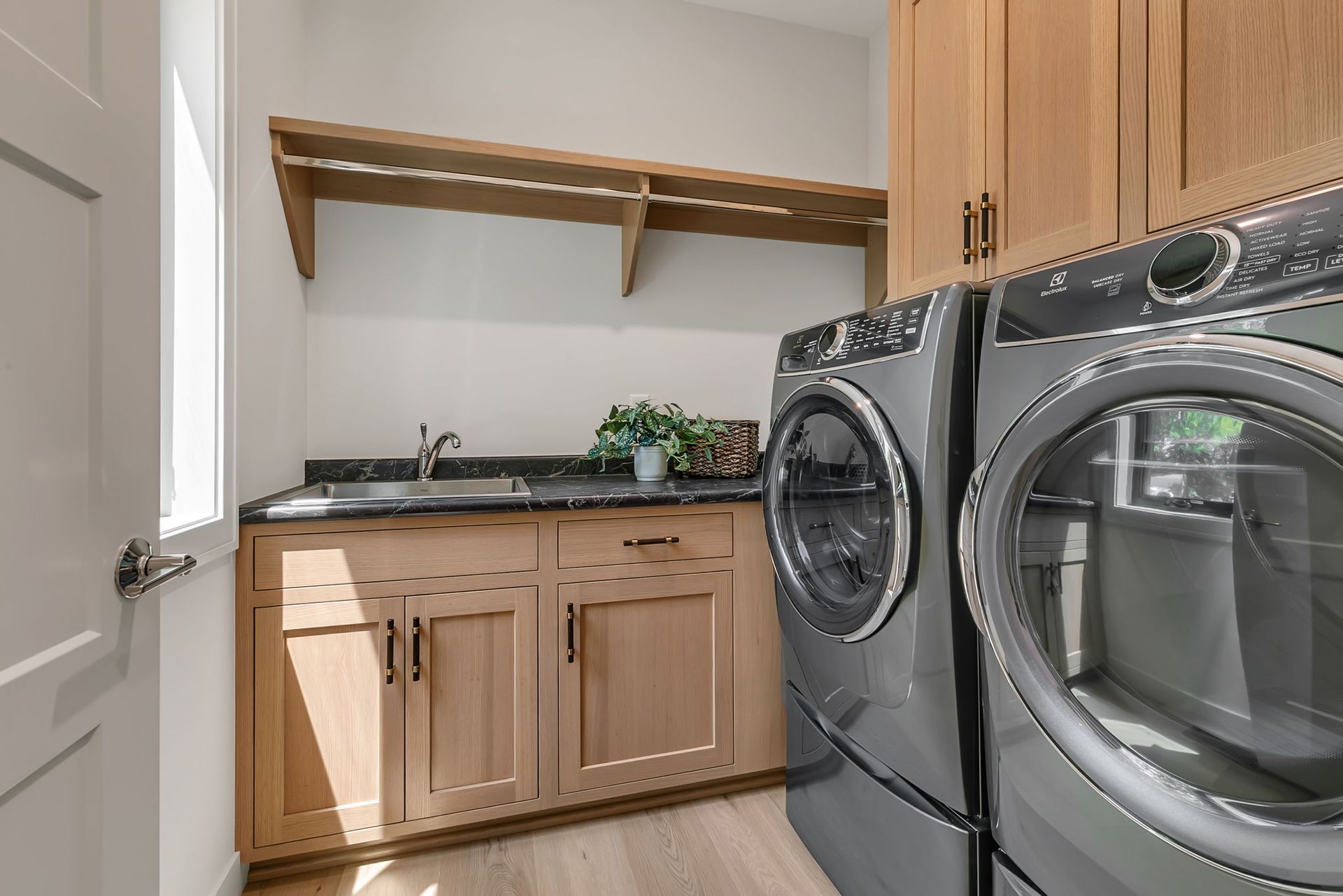 Laundry room with front-loading washer and dryer beside wood cabinets and a shelf over a sink countertop