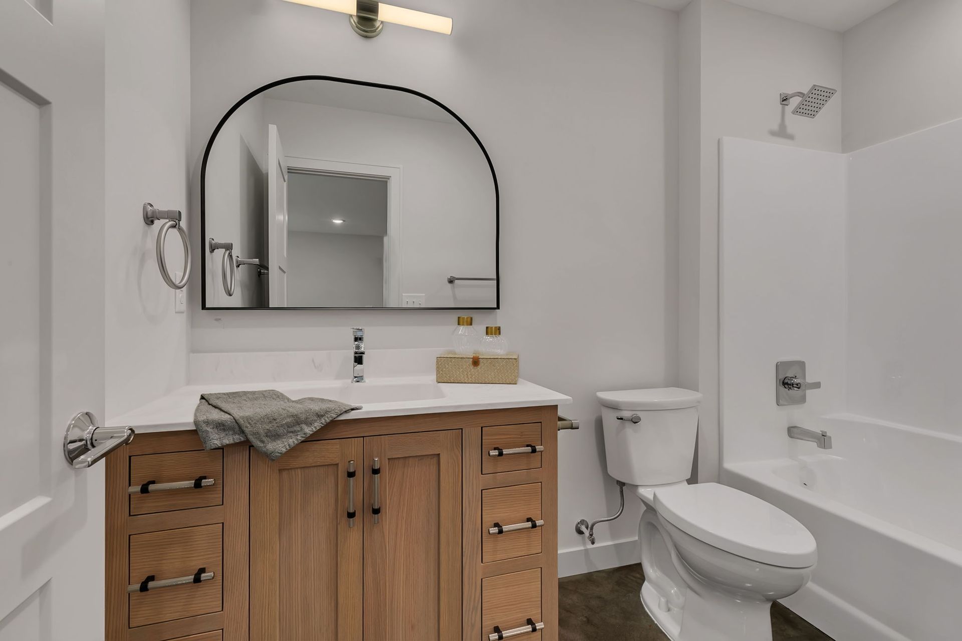 Small bathroom with wood vanity, arched mirror, toilet, and bathtub.