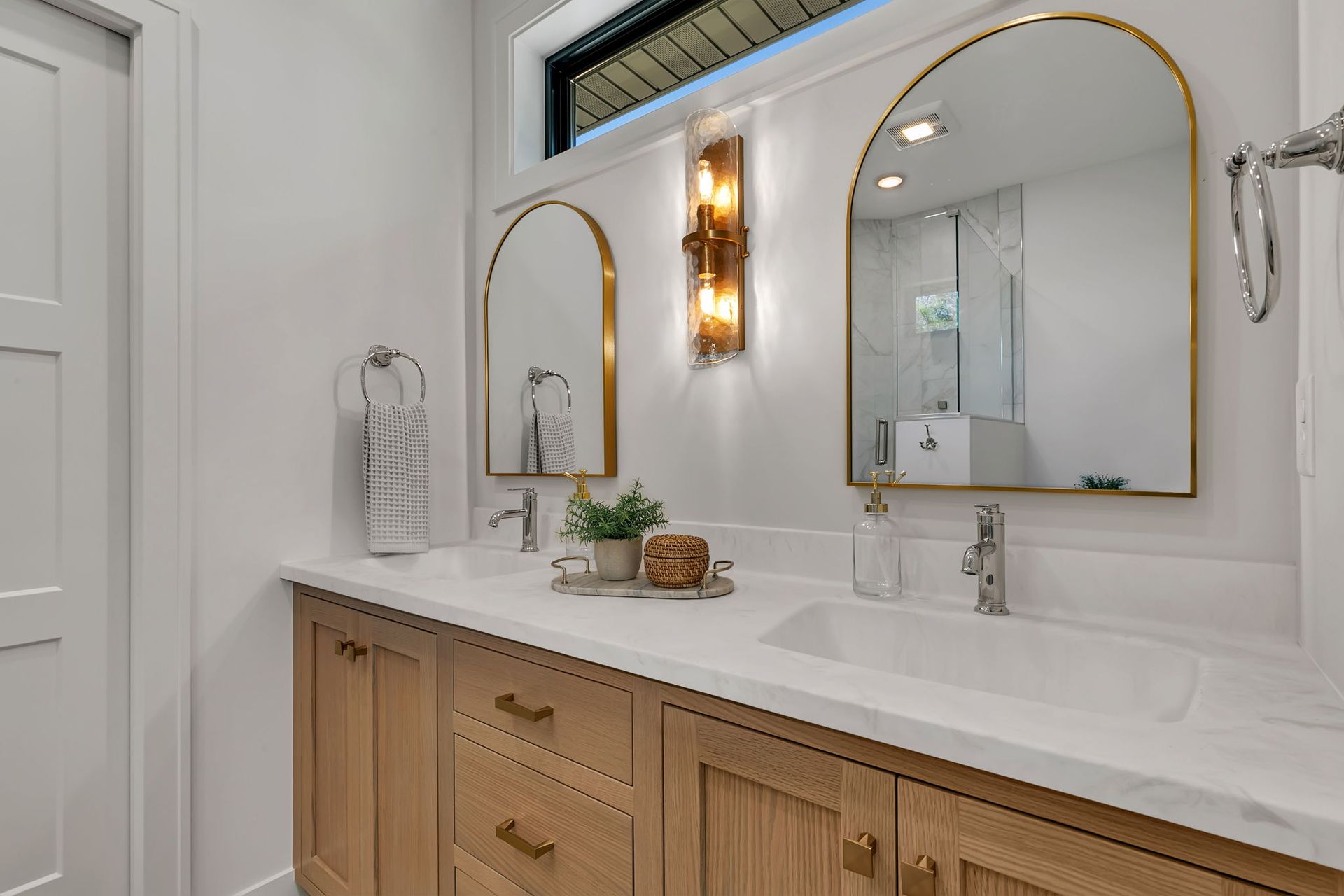 White bathroom vanity with double gold-framed mirrors, wall sconce, and wood cabinets