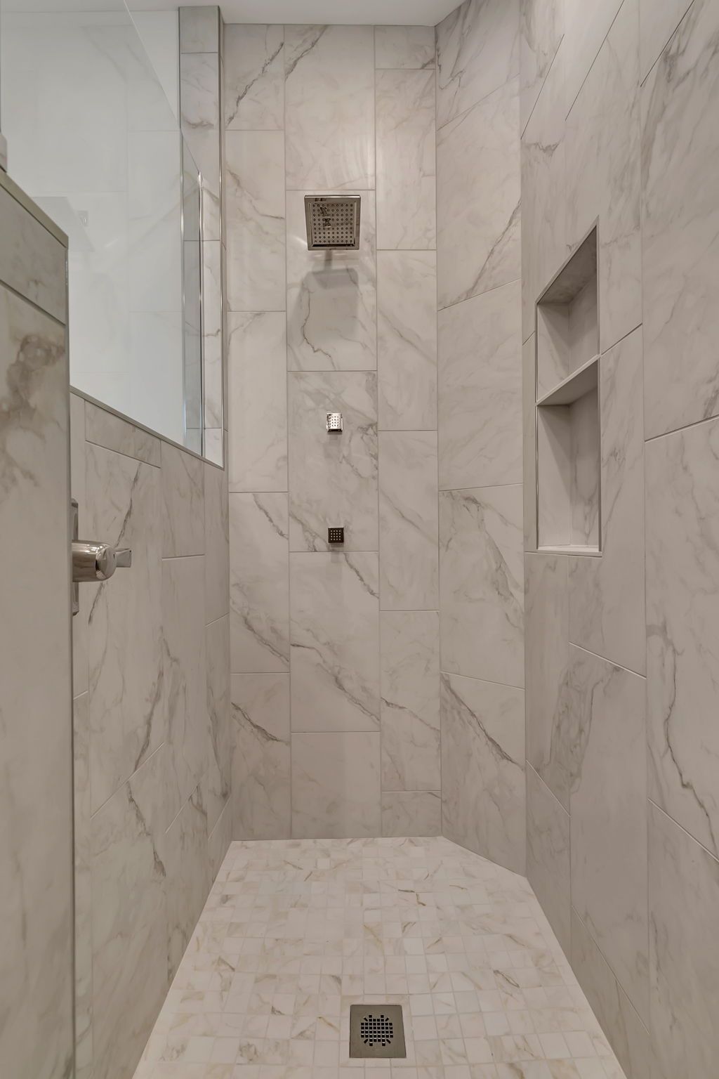 Empty marble-tiled shower with built-in shelves and wall-mounted fixtures